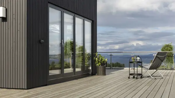 Moderne sort træterrasse med loungestol, glasrækværk og udsigt over vandet ved et stilrent hus