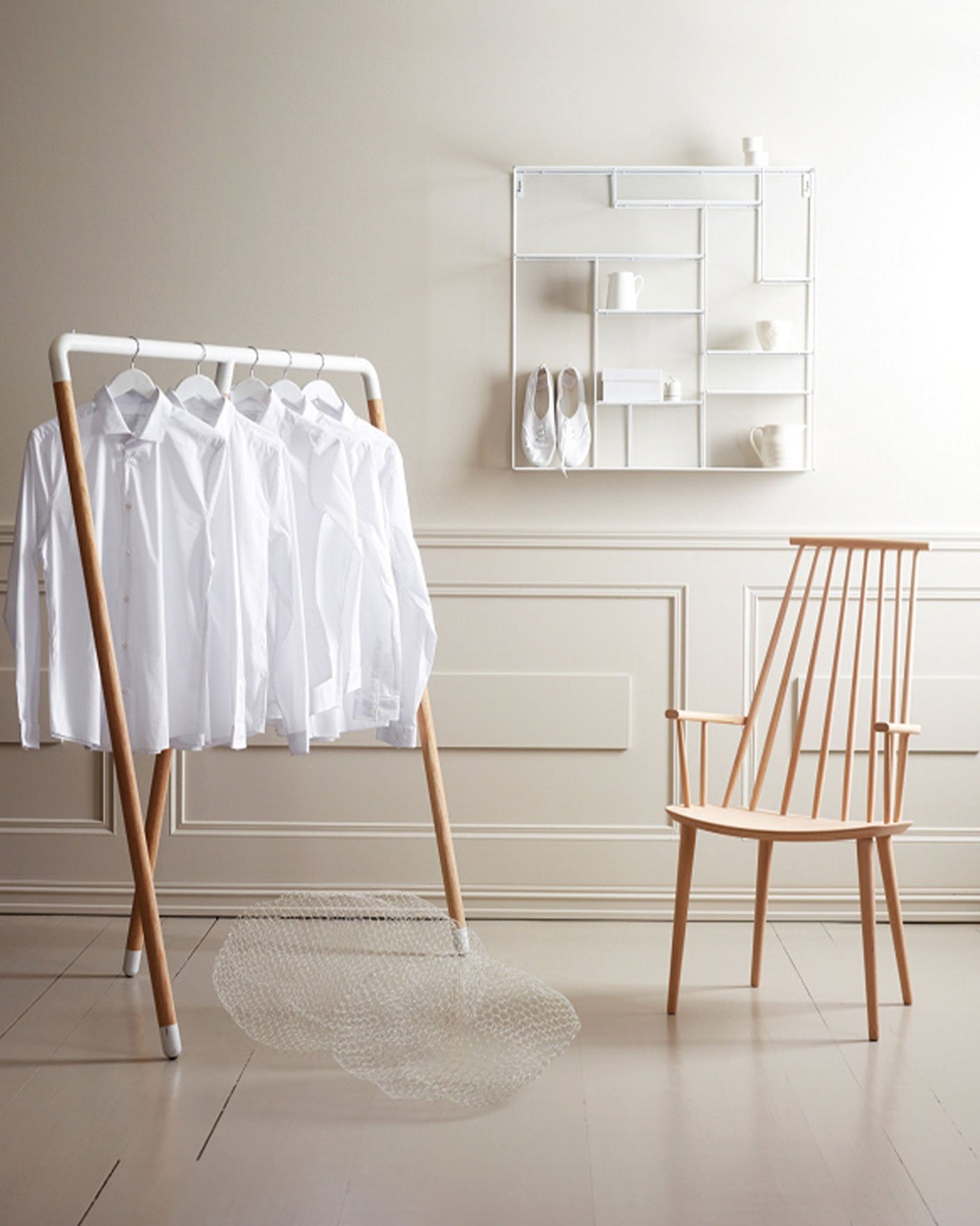 Minimalist space with a wooden chair, white shirts on a rack against a warm muted beige coloured wall painted with Jotun 10341 Limestone.