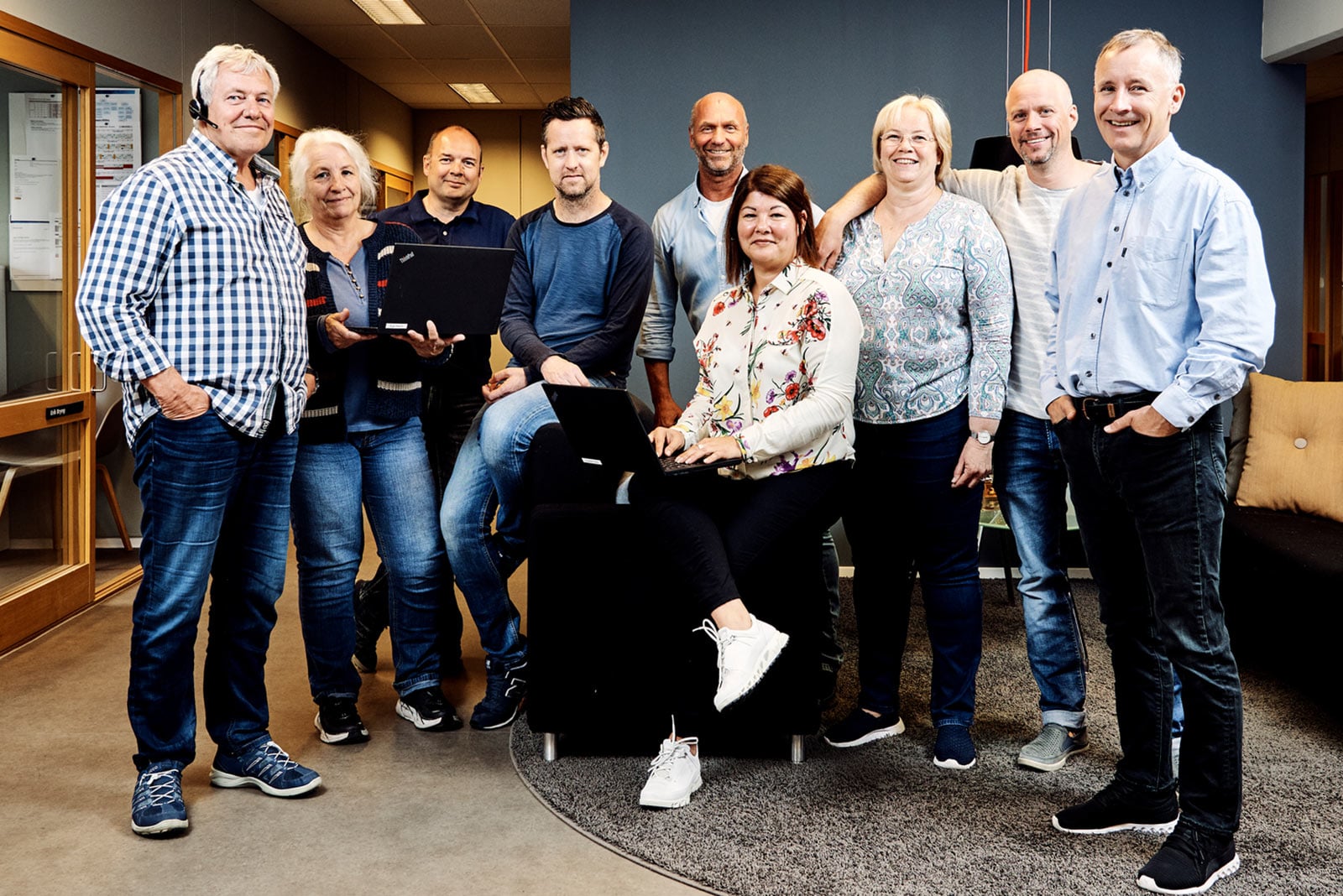 Gruppe mennesker i et kontorlandskap, flere med bærbare datamaskiner, som samarbeider i et moderne arbeidsmiljø.