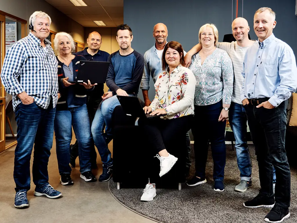 Gruppe mennesker i et kontorlandskap, flere med bærbare datamaskiner, som samarbeider i et moderne arbeidsmiljø.