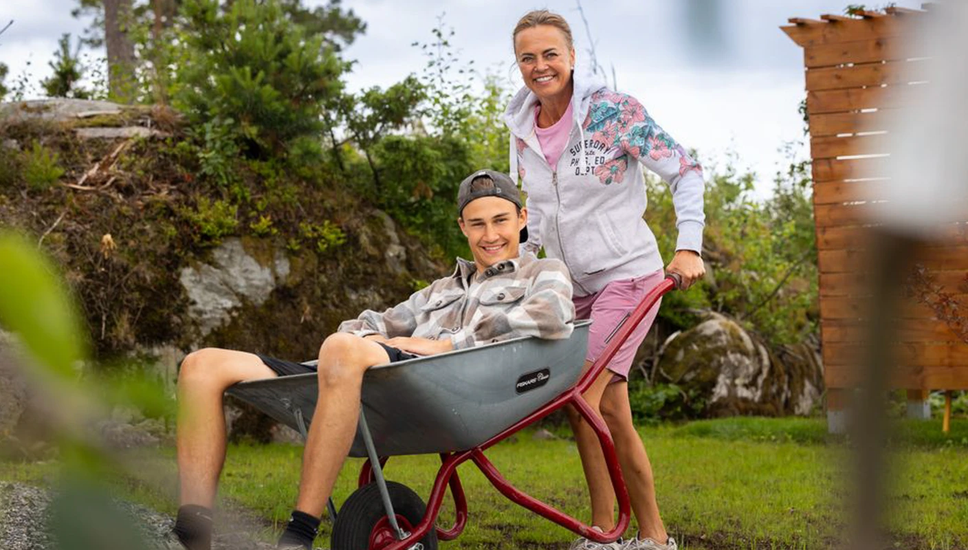 Mor og sønn i den gule sommerhytta, sønn sitter i trillebår som mor skyver. Foto: Espen Solli /TV2.