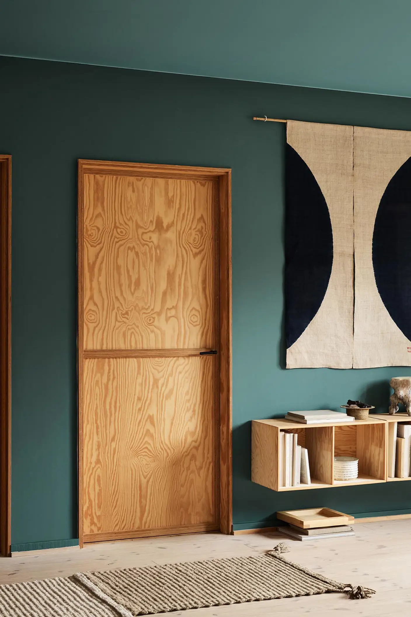 Modern interior with wooden doors, shelf, and decor against a muted, bluish green wall painted in the Jotun colour 6194 Wild Ivy.