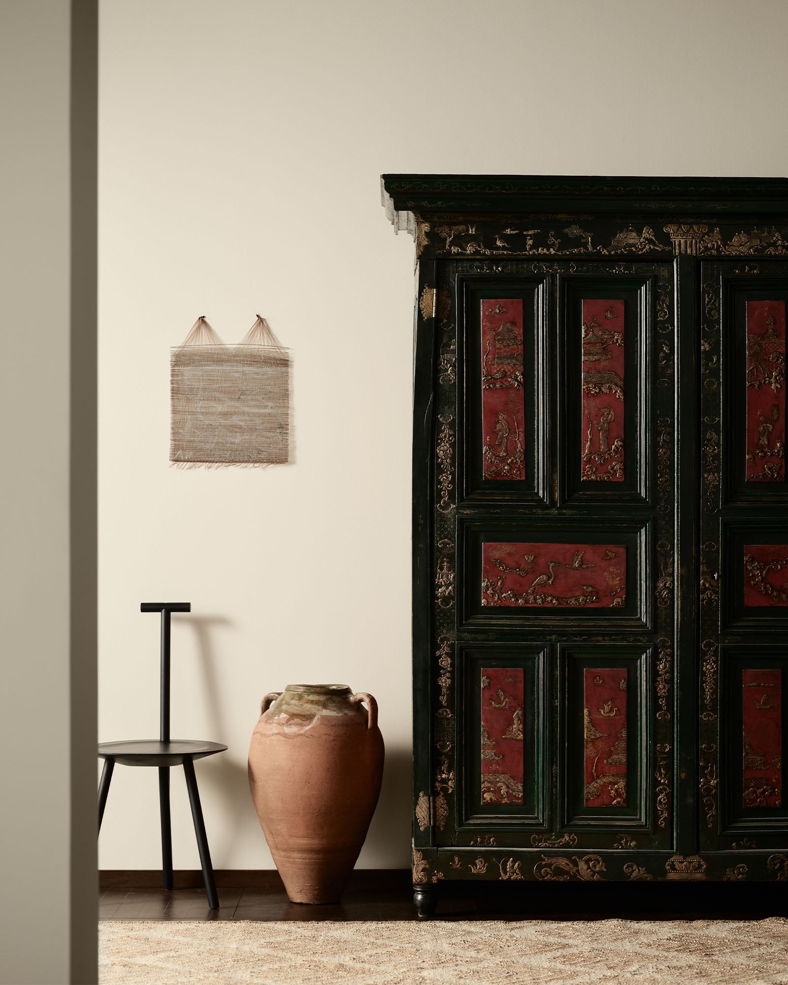 Et skap med røde paneler, en svart krakk og en stor keramisk vase i et minimalistisk rom malt i Jotun fargen 11363 Nostalgic Whisper
