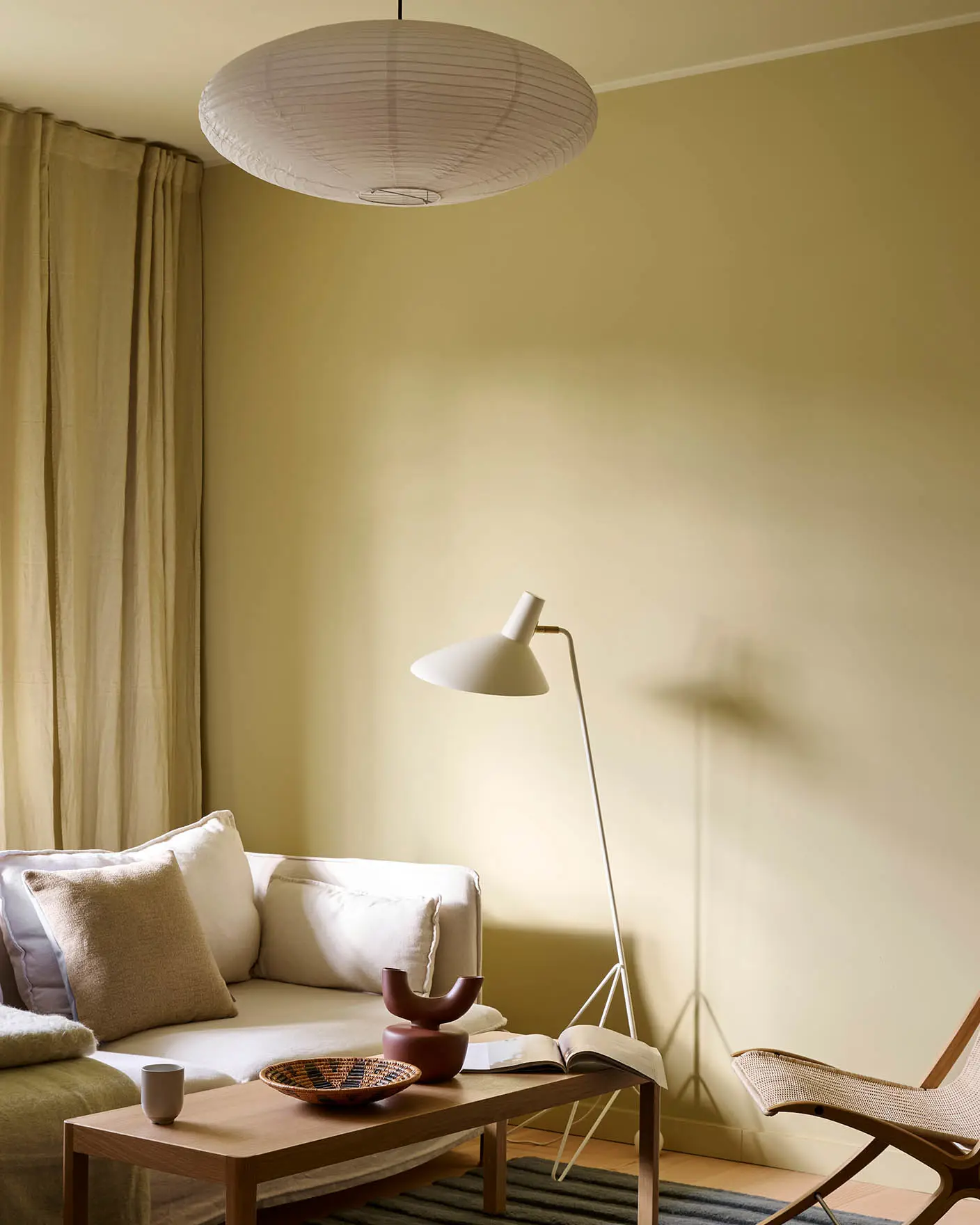 Lys stue med vegger i Jotun Humble Yellow, hvit sofa, beige gardiner og tak malt i Malmø