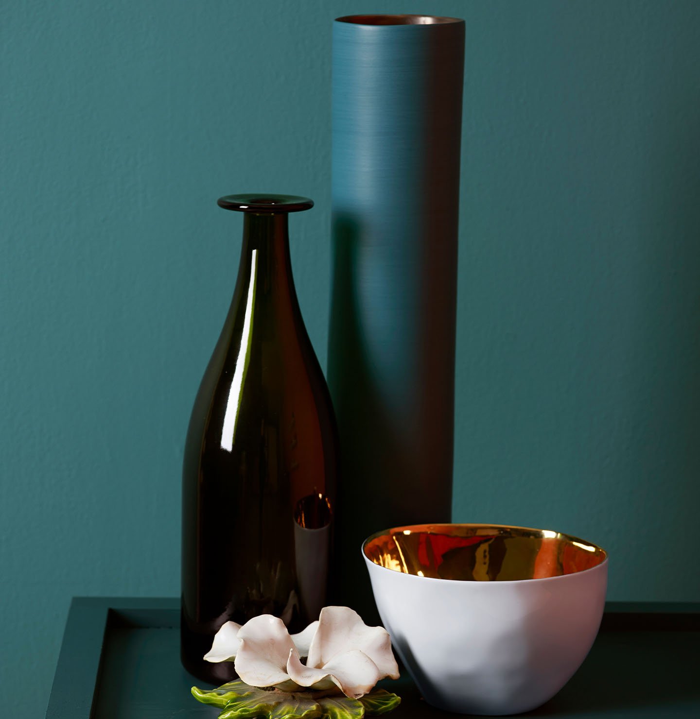 Dark green bedside table with decorations against a muted, greenish blue wall painted with Jotun 5362 Fusion.