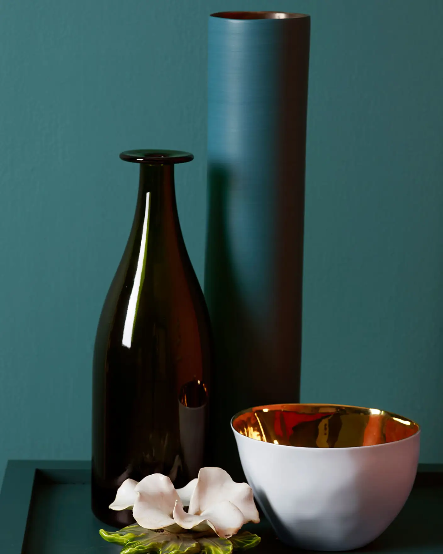 Dark green bedside table with decorations against a muted, greenish blue wall painted with Jotun 5362 Fusion.