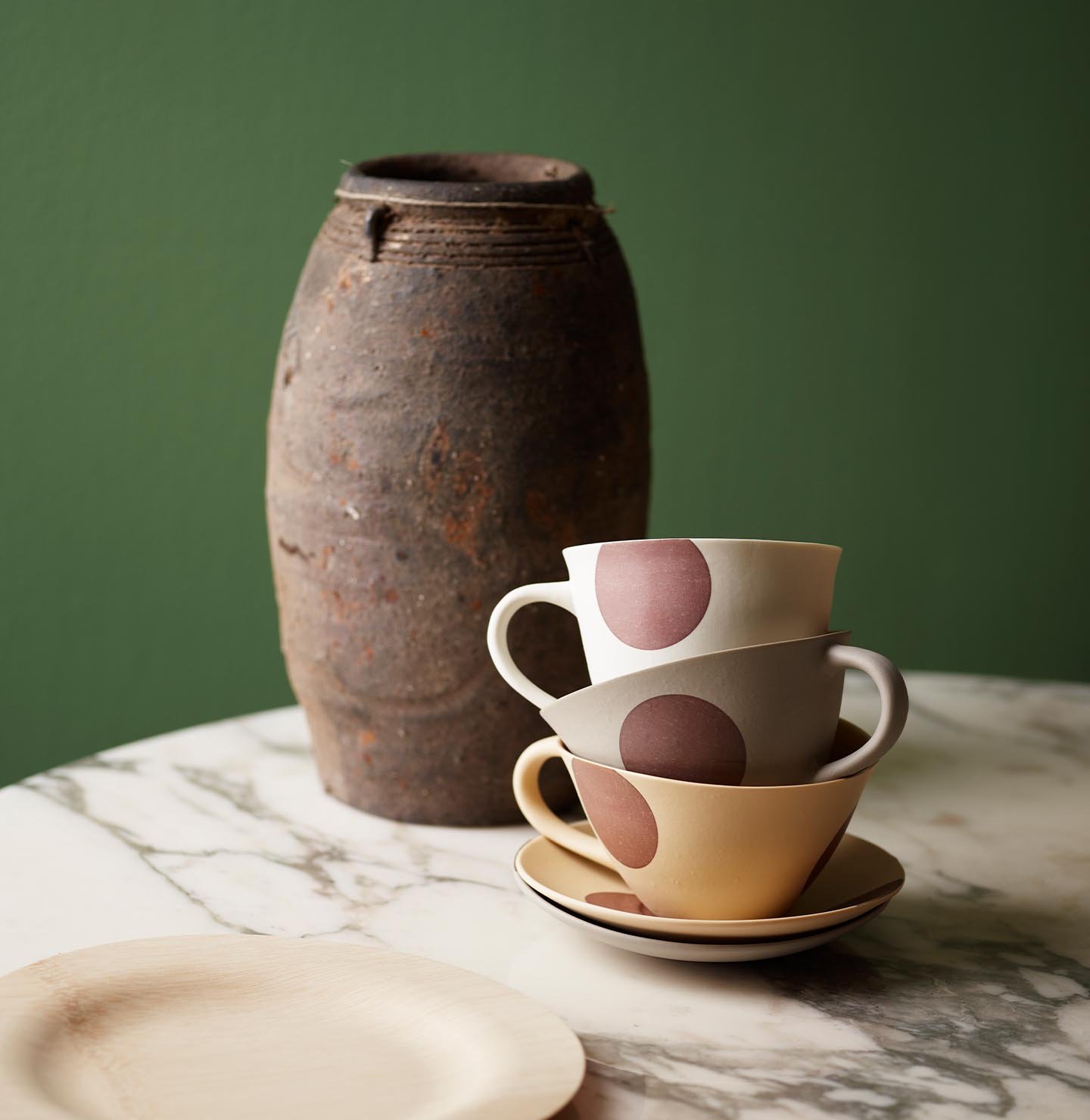 Staplade koppar och rustikt lergods på ett marmorbord, mot en gulgrön vägg målad med Jotun 0125 Palmetto för en ombonad, naturlig känsla.