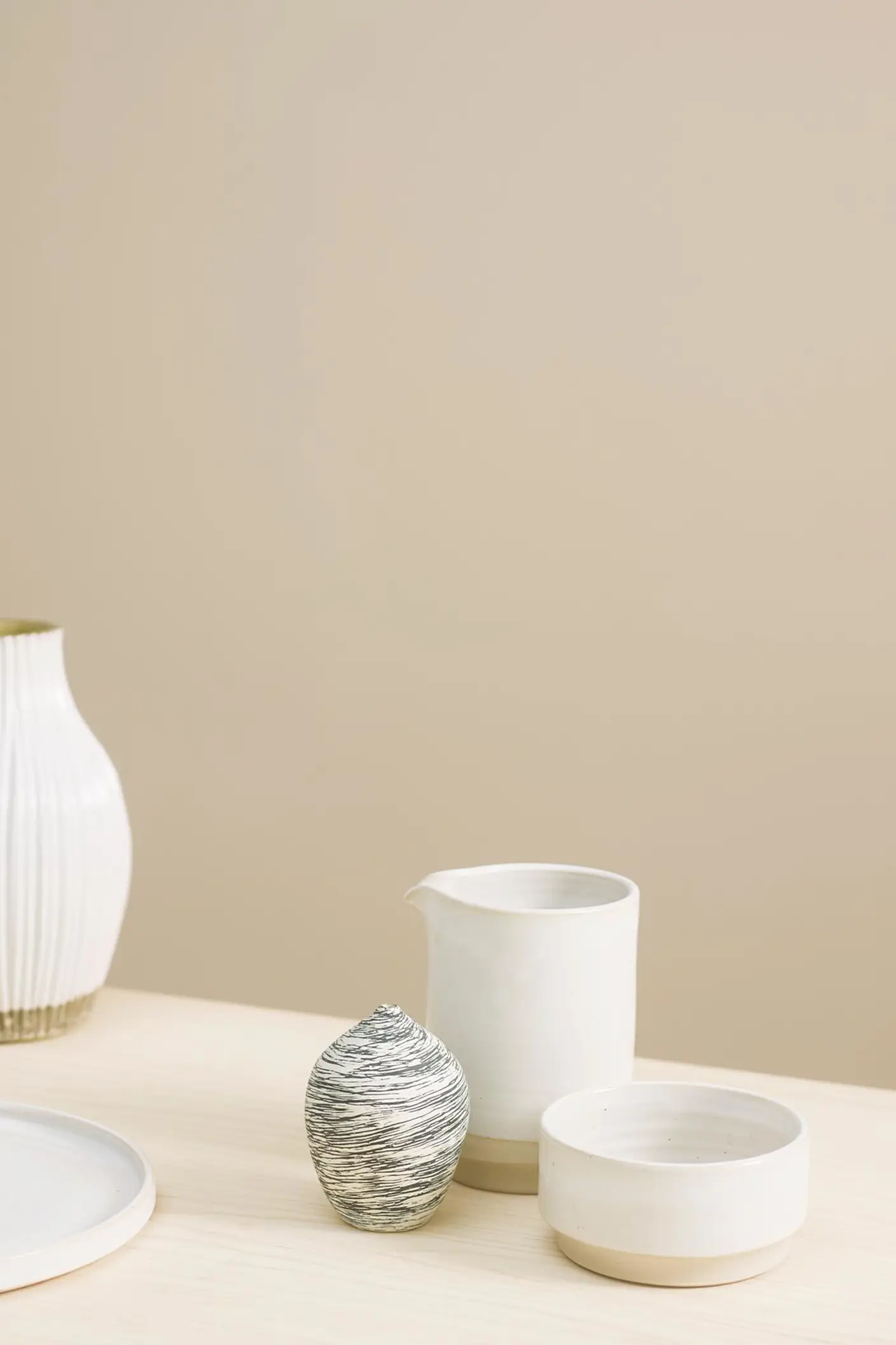 Varm, dämpad beige bakgrund målad i Jotun 1140 Sand tillsammans med ett ljust träbord skapar en naturlig bakgrund för minimalistisk keramik.
