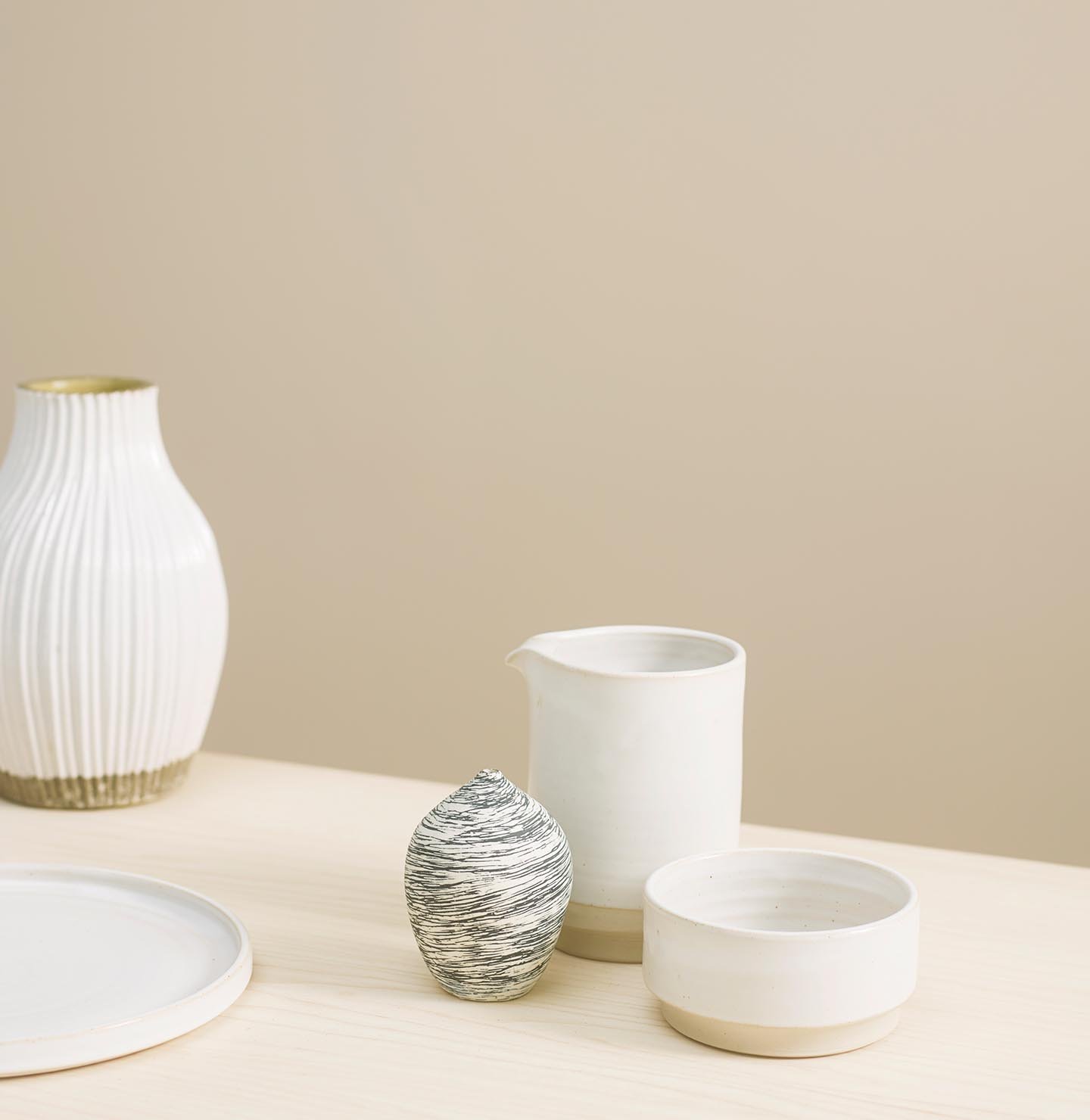 Varm, dämpad beige bakgrund målad i Jotun 1140 Sand tillsammans med ett ljust träbord skapar en naturlig bakgrund för minimalistisk keramik.