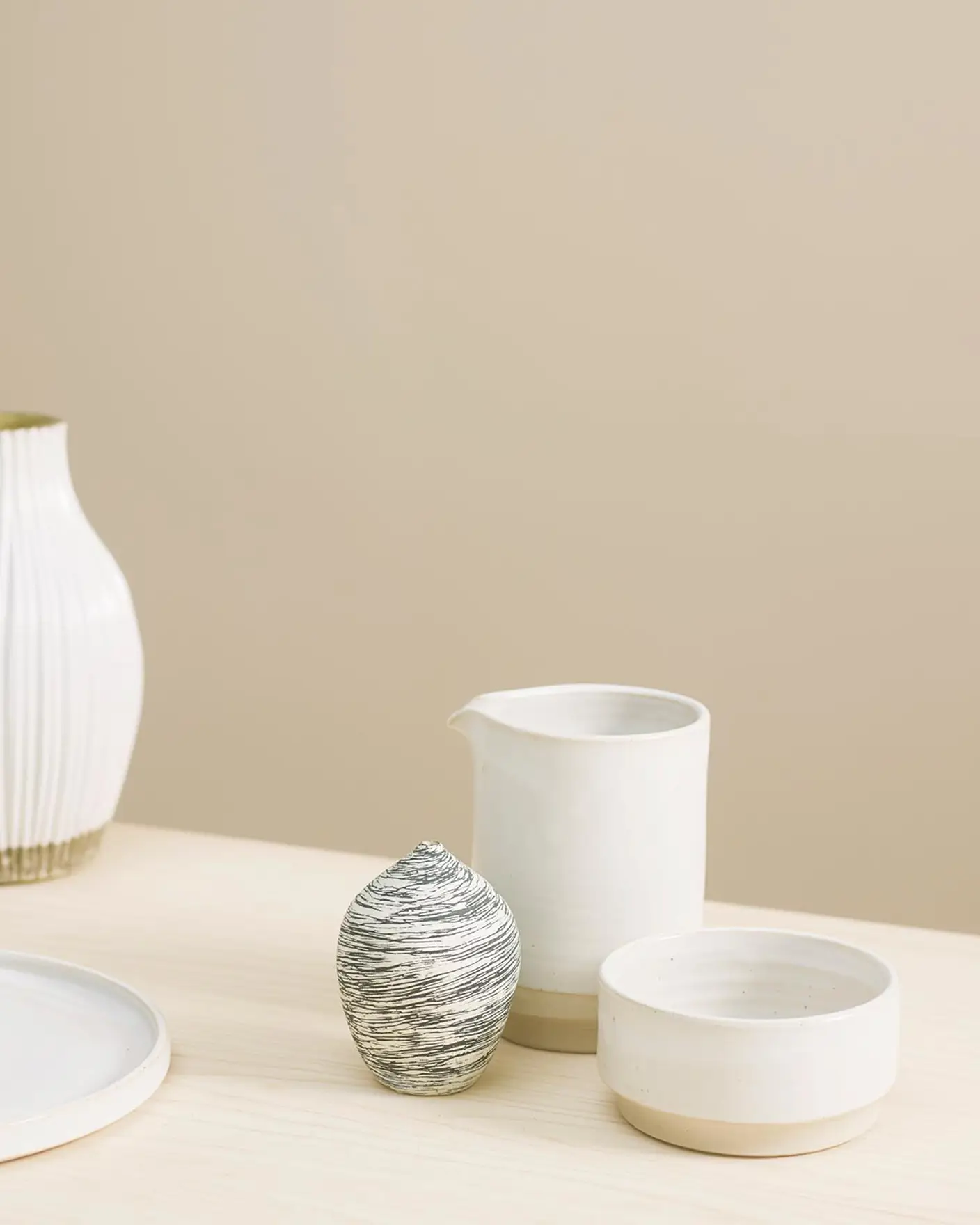 Varm, dämpad beige bakgrund målad i Jotun 1140 Sand tillsammans med ett ljust träbord skapar en naturlig bakgrund för minimalistisk keramik.