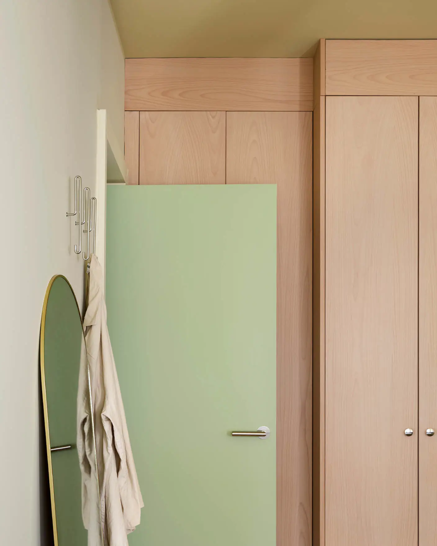 Dør i fargen Avocado Green foran høye skap i lyst tre. Veggene er malt i Jotun Malmø, og taket i Earthy Yellow.