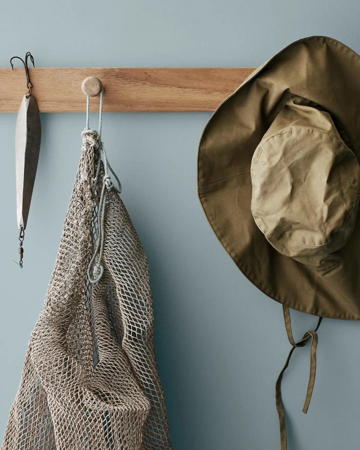 Ett trälist med ett fiskedrag, ett nät och en olivgrön hatt, mot en dämpad blå vägg målad med Jotun 4894 Ocean Air, som ger en luftig, kustnära känsla.