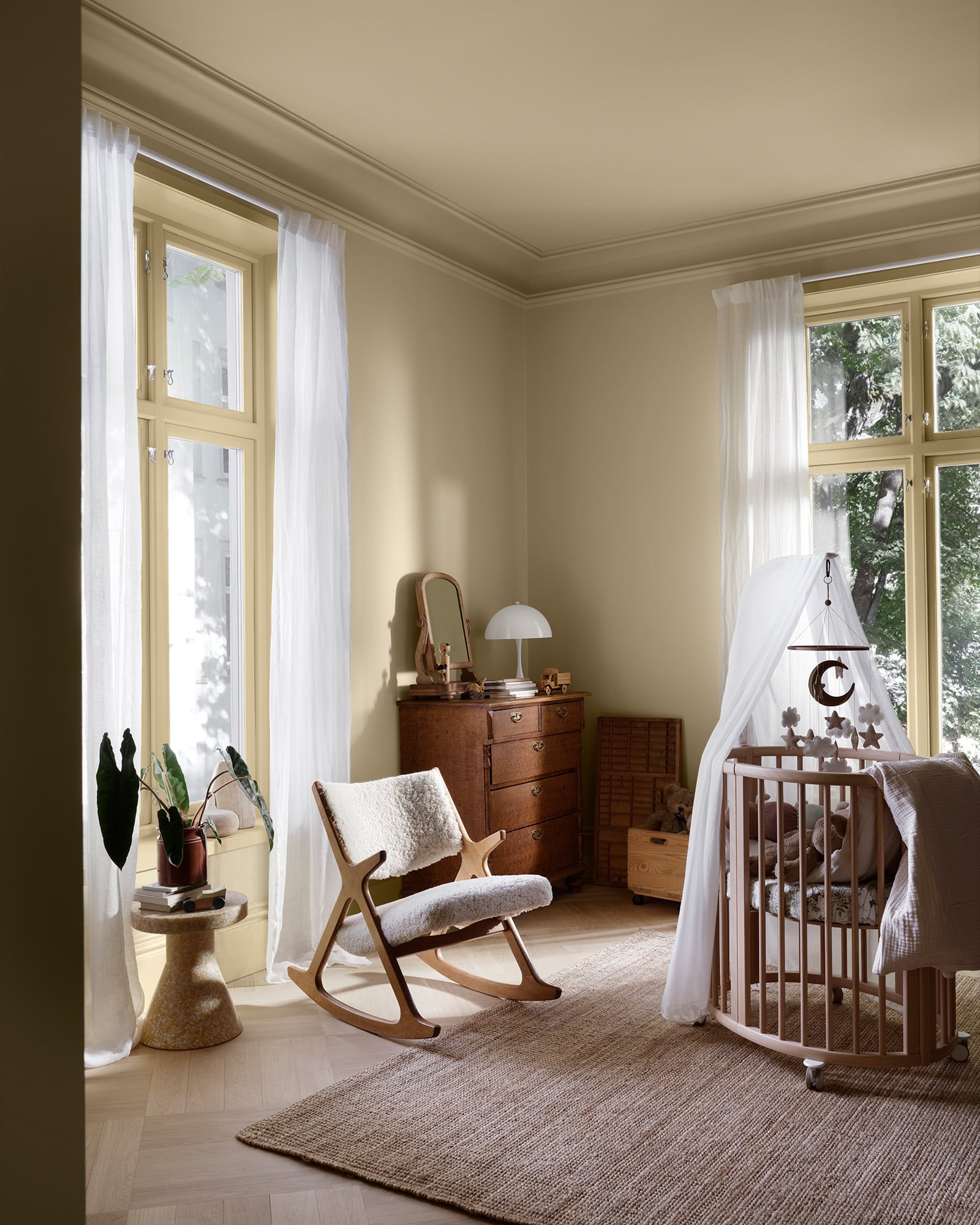 Lyst barnerom malt med LADY New era i fargen Hazy yellow med tremøbler, gyngestol, sprinkelseng og store vinduer med hvite gardiner i naturlig dagslys