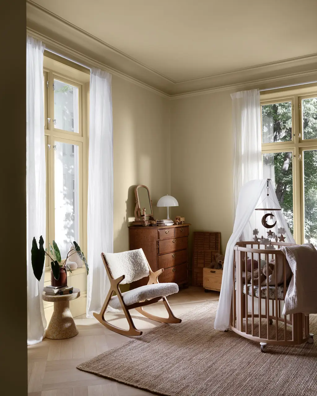 Lyst barnerom malt med LADY New era i fargen Hazy yellow med tremøbler, gyngestol, sprinkelseng og store vinduer med hvite gardiner i naturlig dagslys