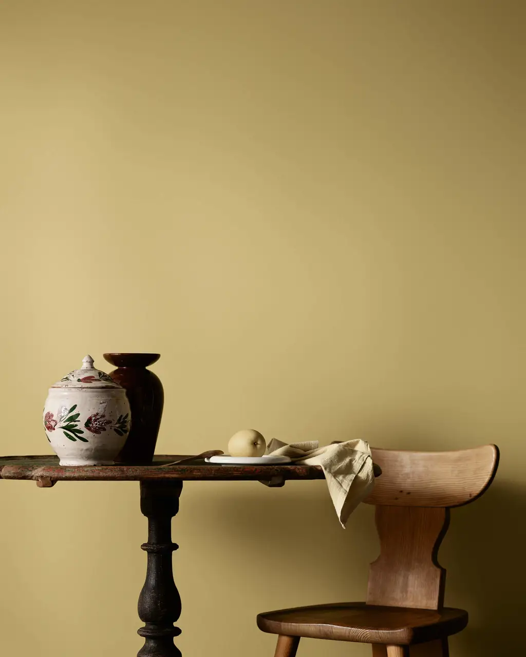 Et rustikt trebord og en stol med keramiske vaser mot en kjøkkenvegg malt gul i Jotun 1627 Retro