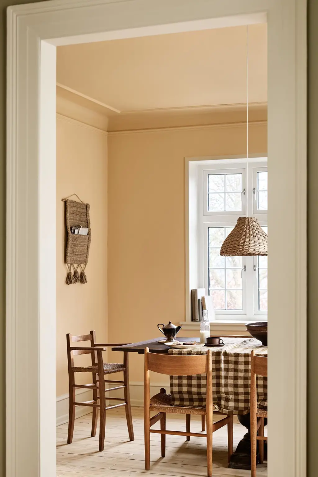 Dining area with a checkered tablecloth, wooden chairs, and ochre coloured walls and ceiling painted with Jotun's 11202 Mild Ochre.