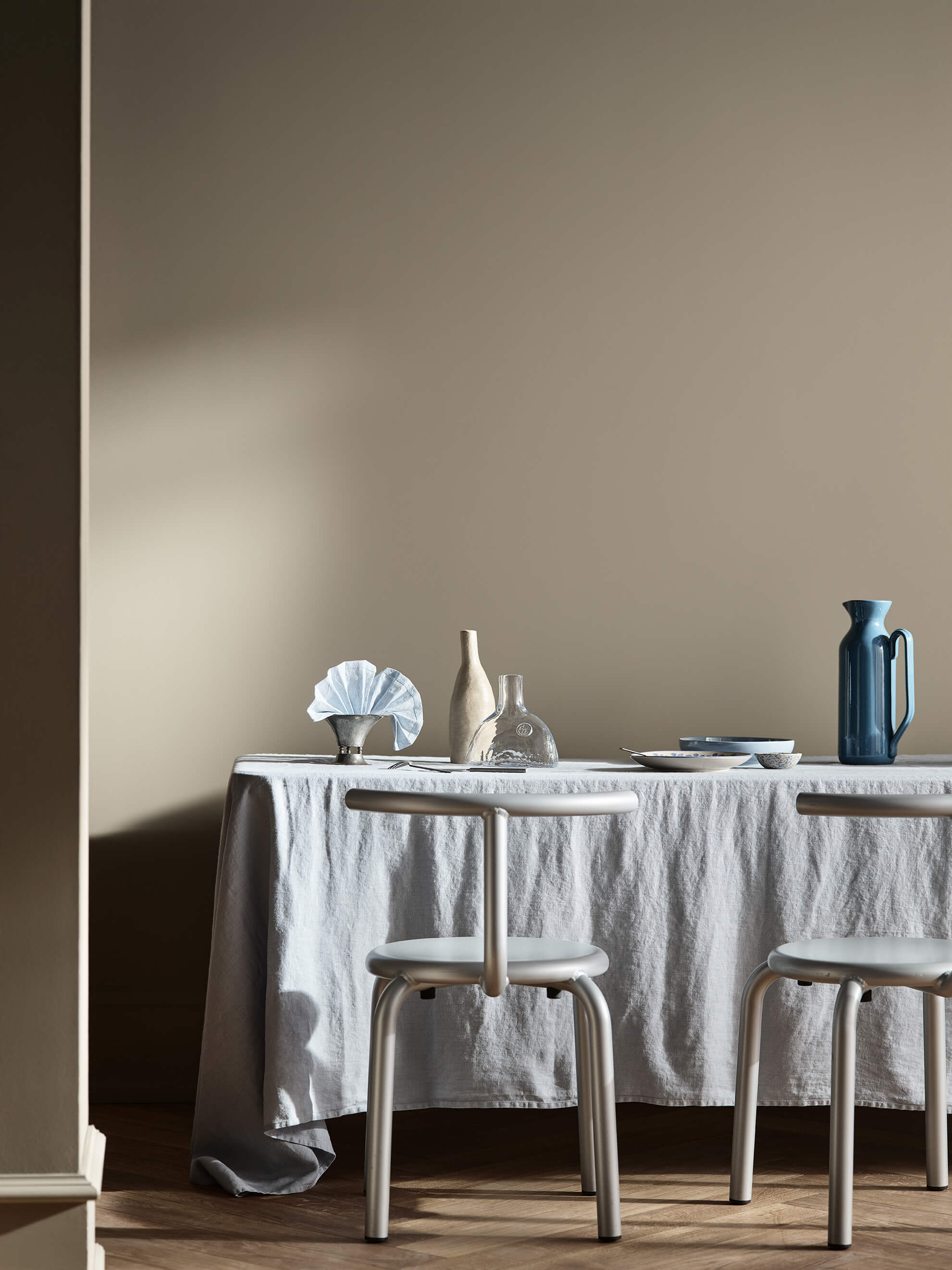 Et spisebord med blå og klare glaskander foran beige vægge malet i Jotun 10966 Almond Beige.