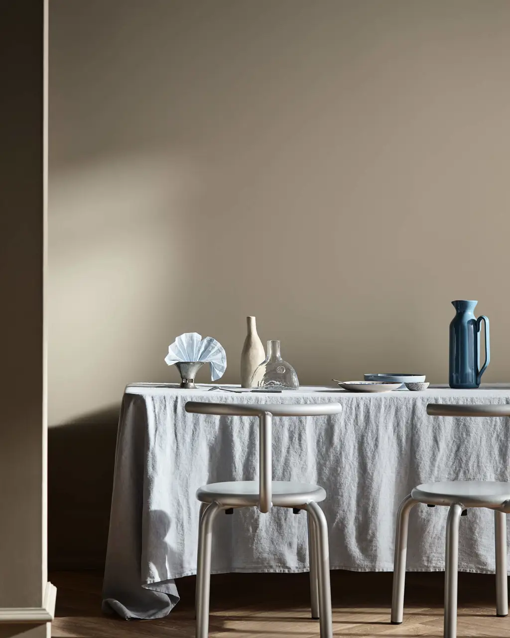 Et spisebord med blå og klare glasskanner foran beige vegger malt i Jotun 10966 Almond Beige