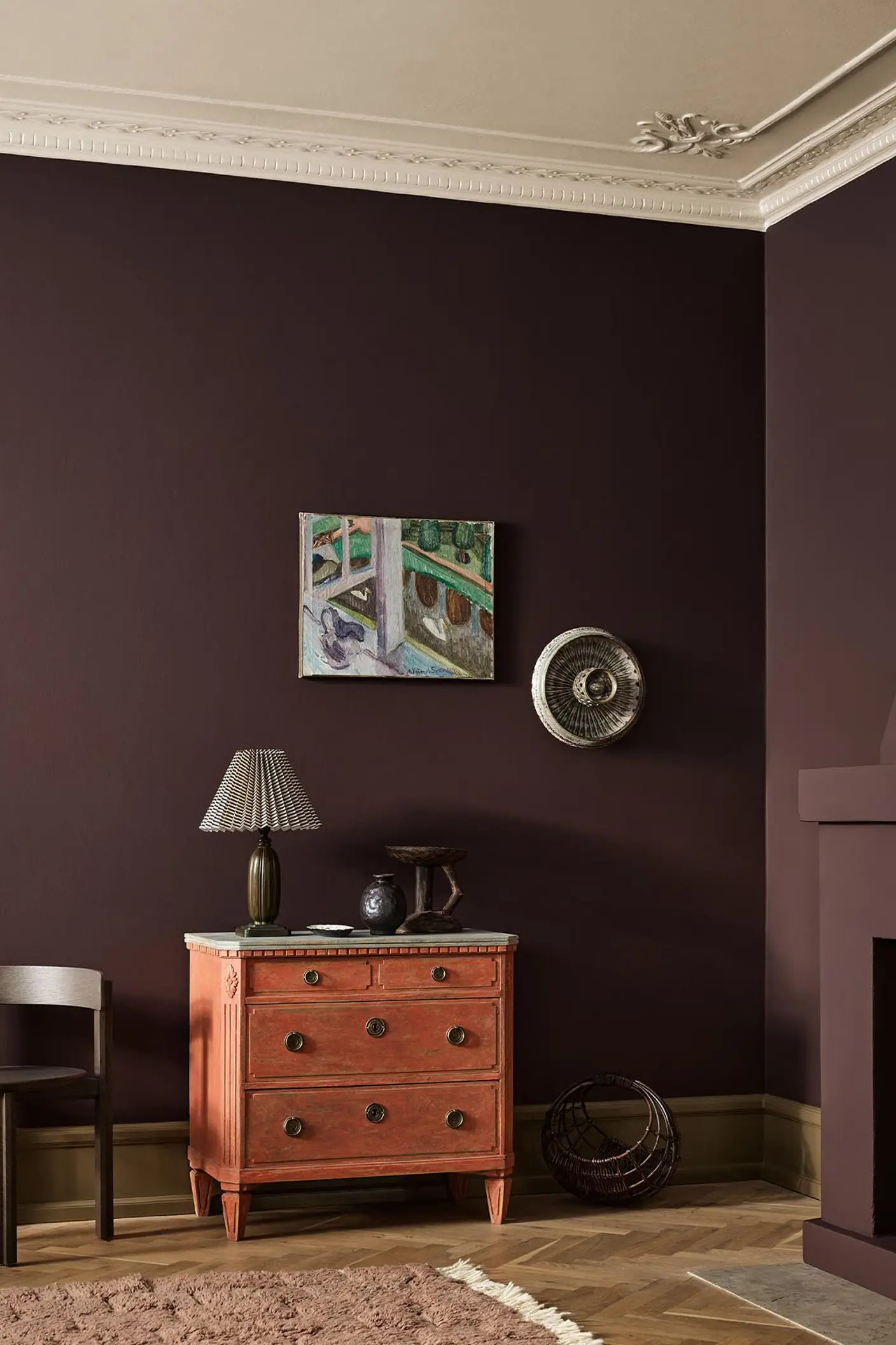 A red dresser, wall art, and fireplace against a deep, brownish red wall painted with the colour Jotun 2149 Coffee.