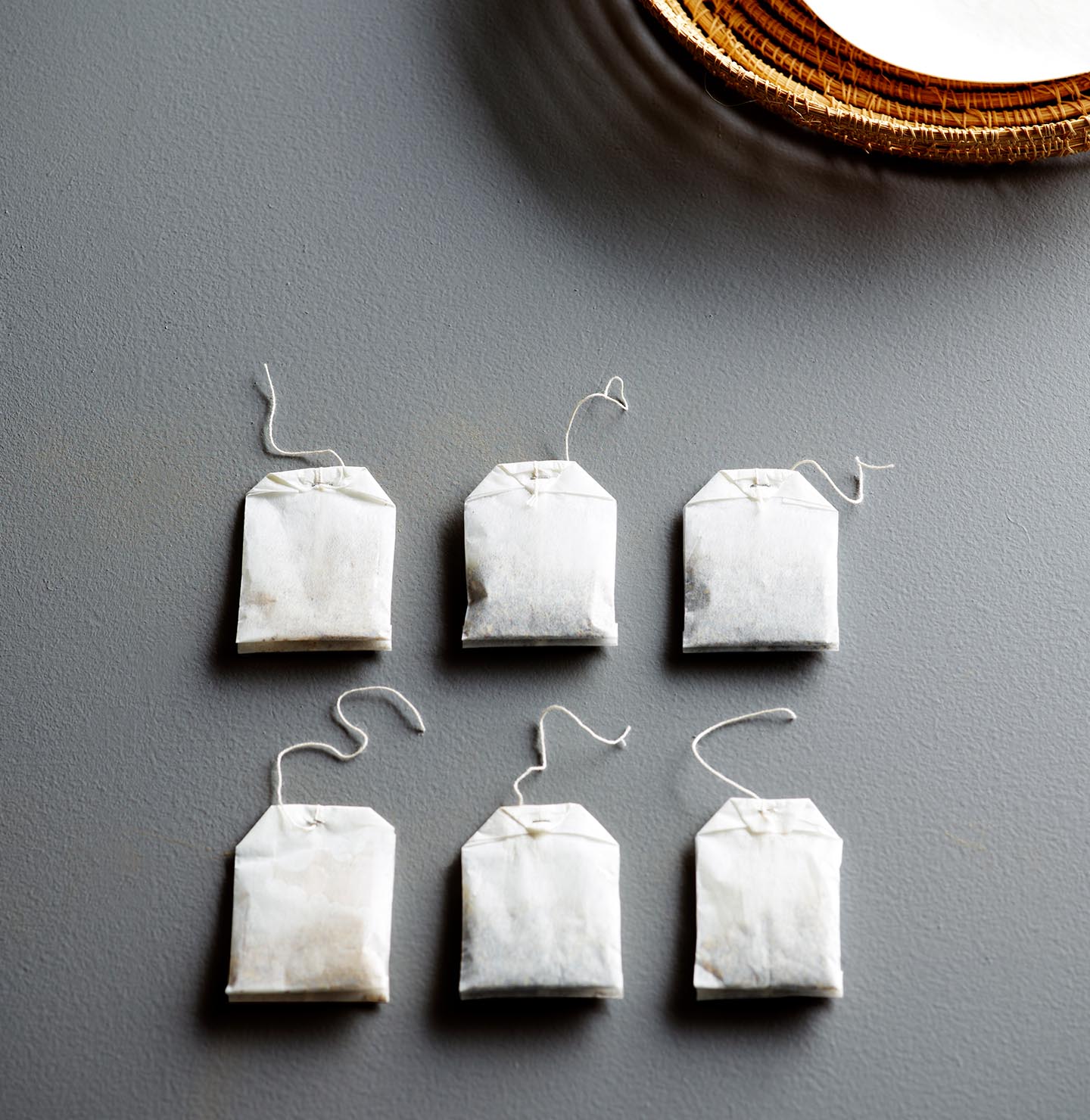 Teposer er pent ordnet på en strukturert, blågrå overflate malt med fargen Jotun 4629 Skyggeblå, ved siden av en vevd tallerken, og skaper en rolig, minimalistisk stemning.