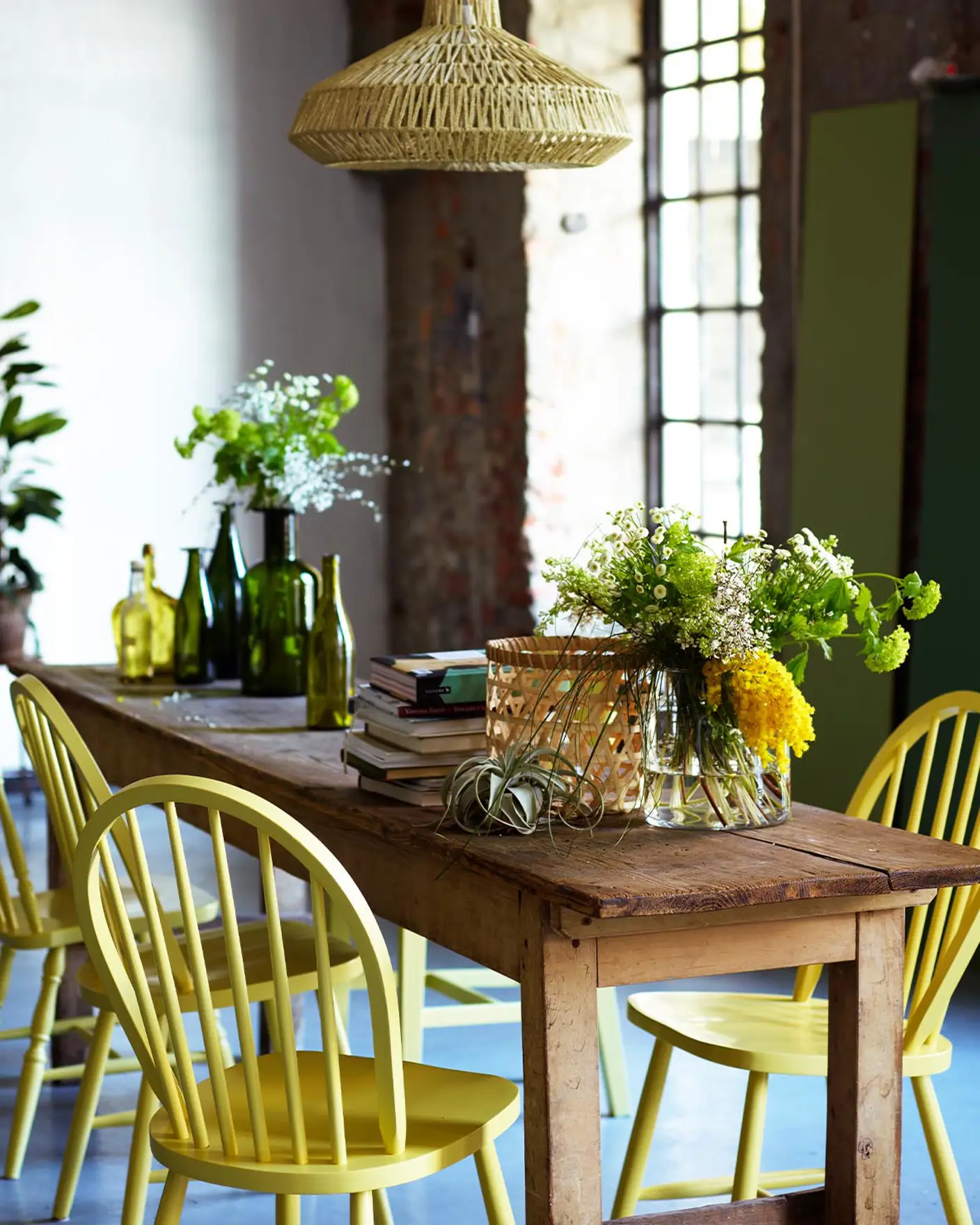 Rustik matplats med stolar målade i en frisk gul nyans, färgen 10235 Summarsol från Jotun, omgiven av mjuka gröna toner och industriella texturer.