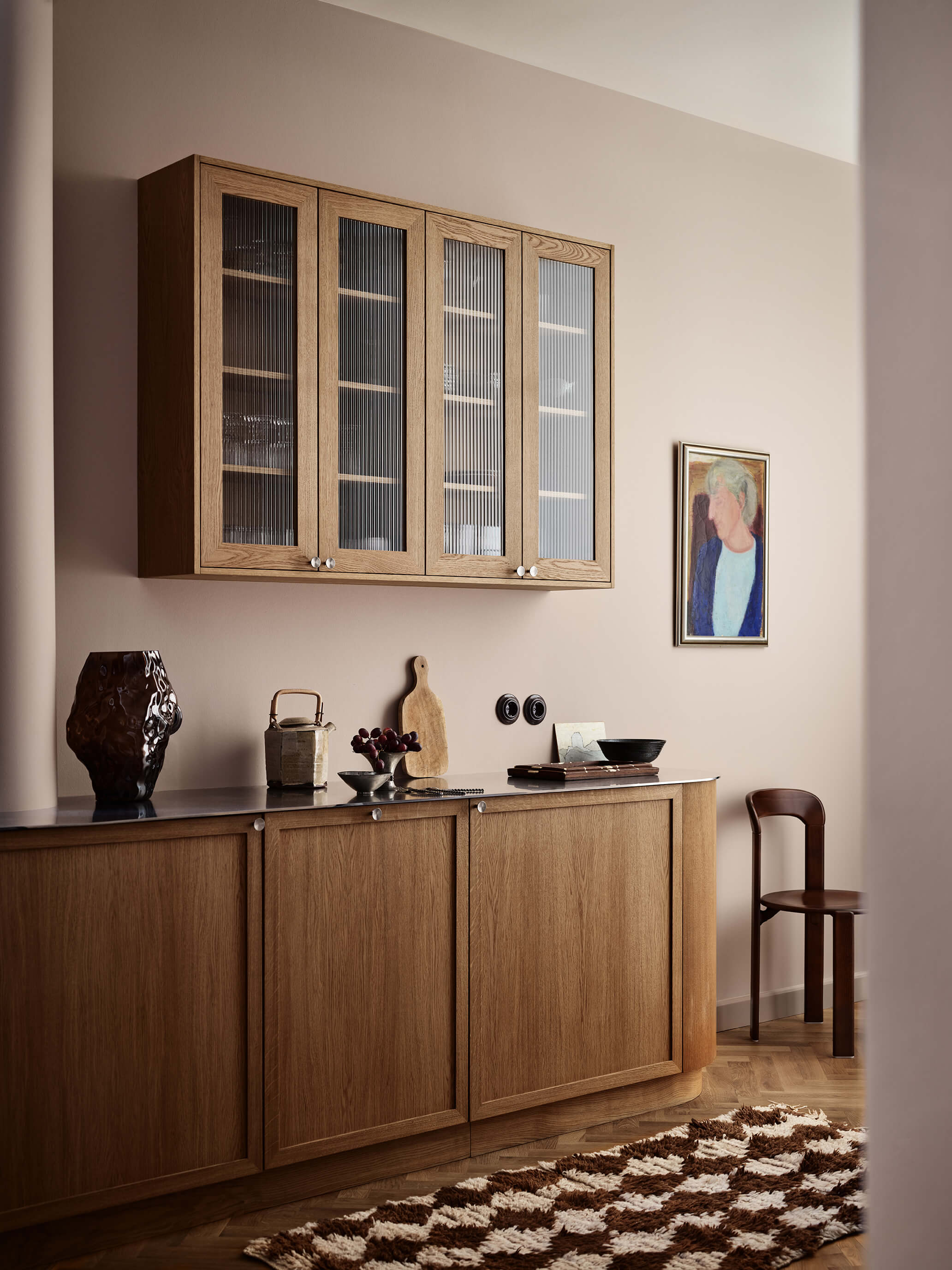 Et kjøkkenområde med eikeskap og et teppe med struktur mot vegger malt i dus pudderrosa i Jotun 20185 Friendly Pink og tak i beige Jotun 1281 Pearl Beige