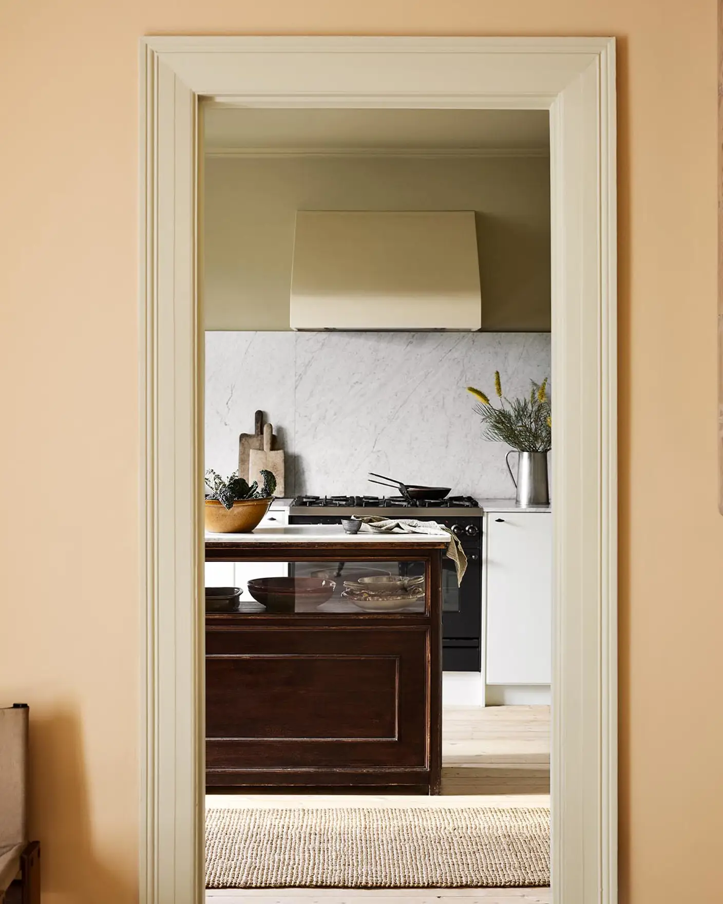 Kitchen viewed through a doorway. The wall in front is painted in the pale, ochre yellow colour 11202 Mild Ochre from Jotun.