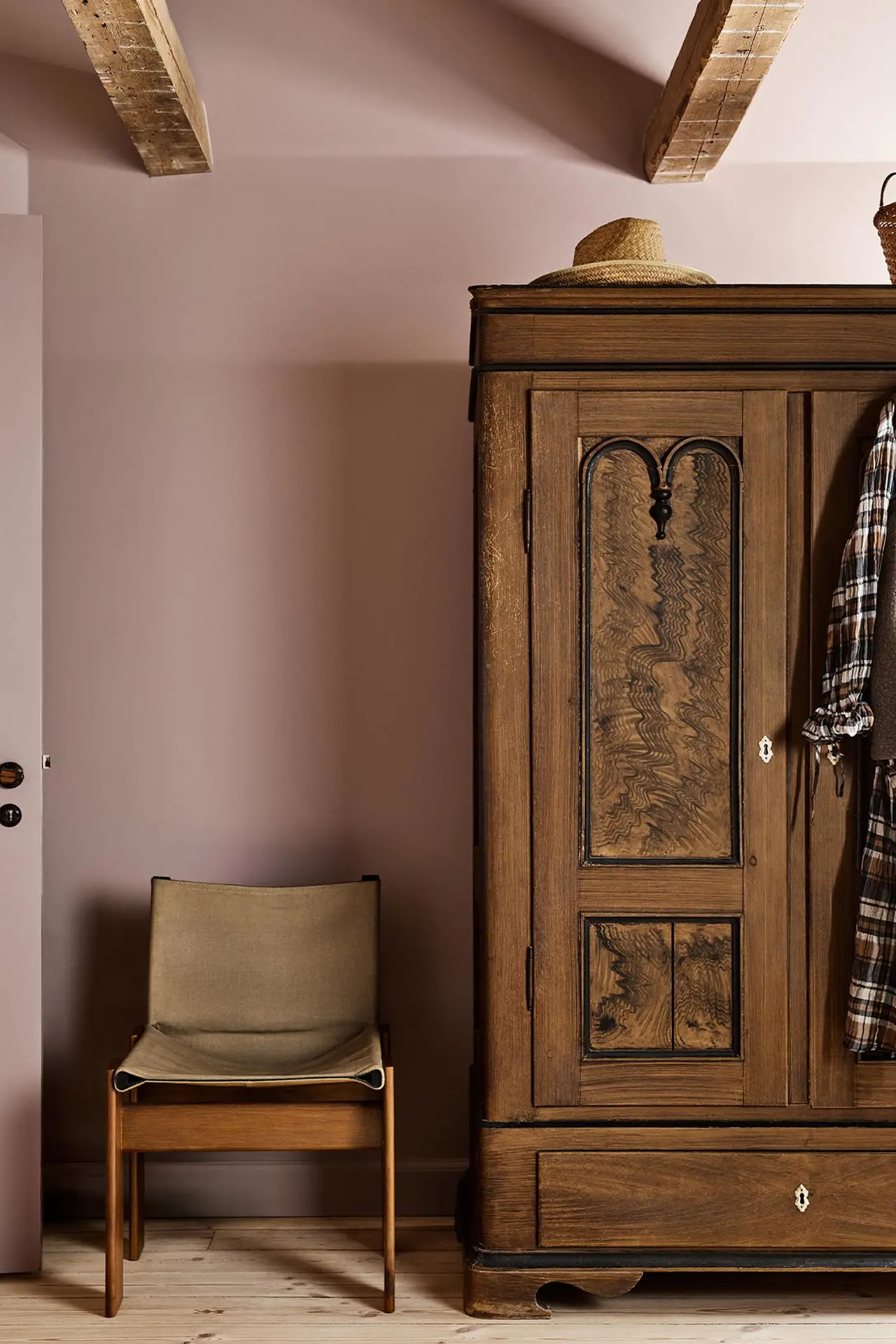 Bedroom with a wooden wardrobe and chair against a muted pink wall painted with Jotun's colour 20054 Silky Pink.
