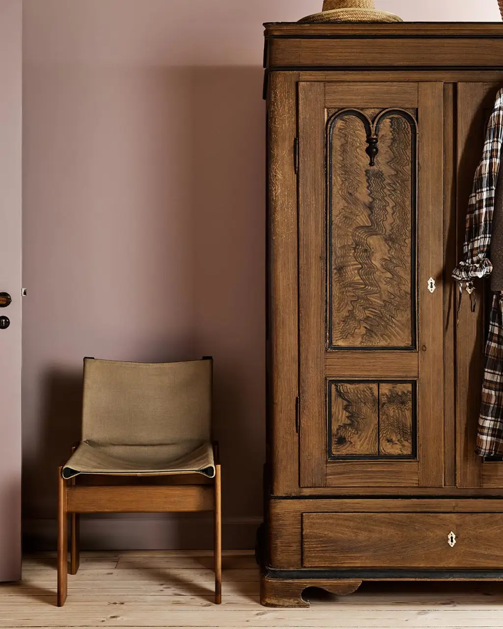 Bedroom with a wooden wardrobe and chair against a muted pink wall painted with Jotun's colour 20054 Silky Pink.