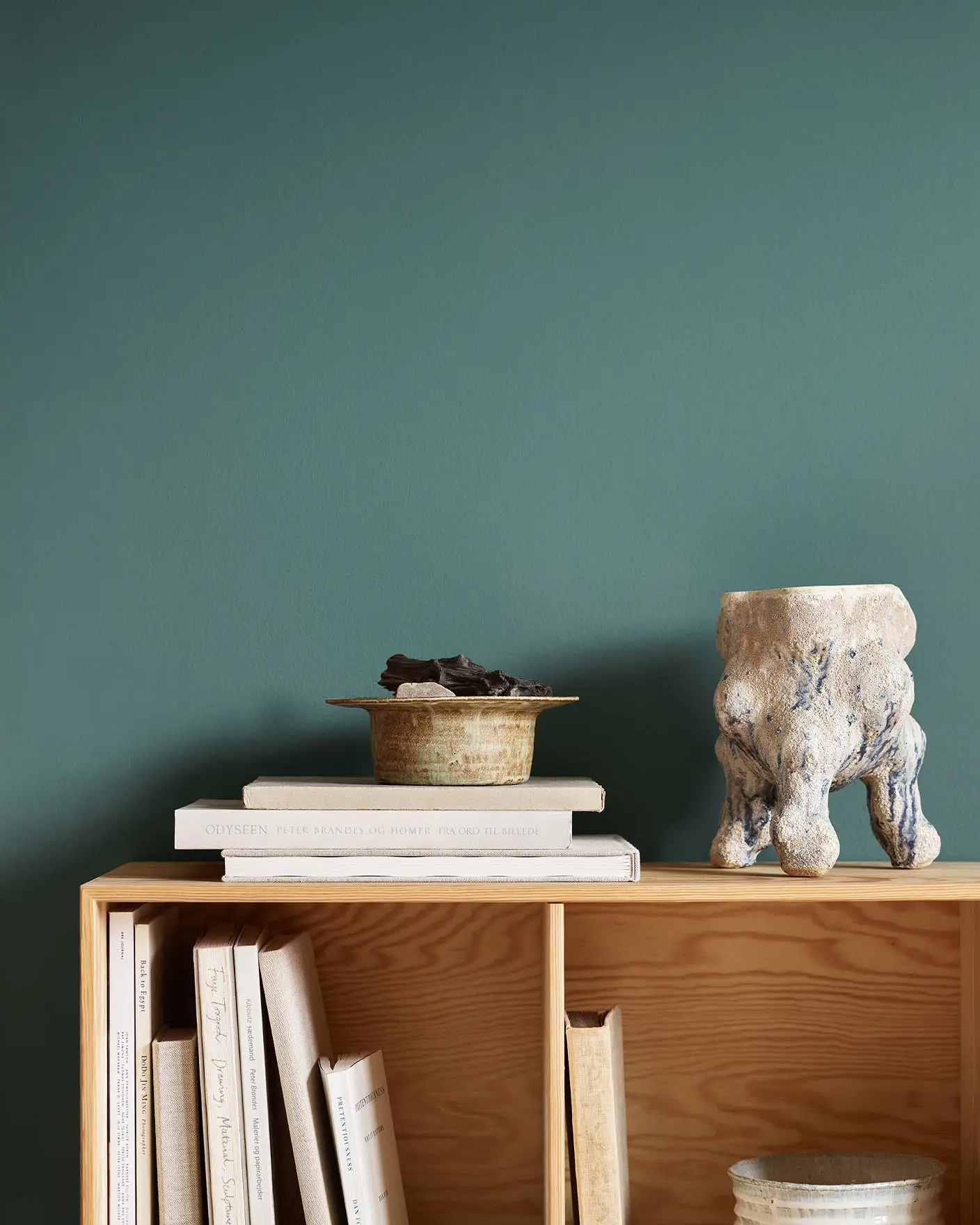 Bookshelf with stacked books, bowl, and ceramic sculpture against a green wall painted in the Jotun colour 6194 Wild Ivy.
