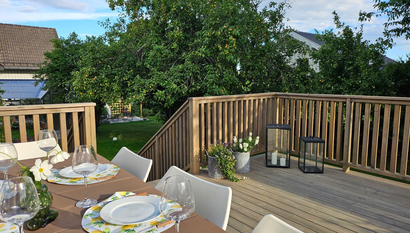 Terrasse beiset med Trebitt Terrassebeis i den lune og beige Nordisk Tre. Utelykter står i et hjørne, mens et utebord er dekket til et sommerlig måltid.