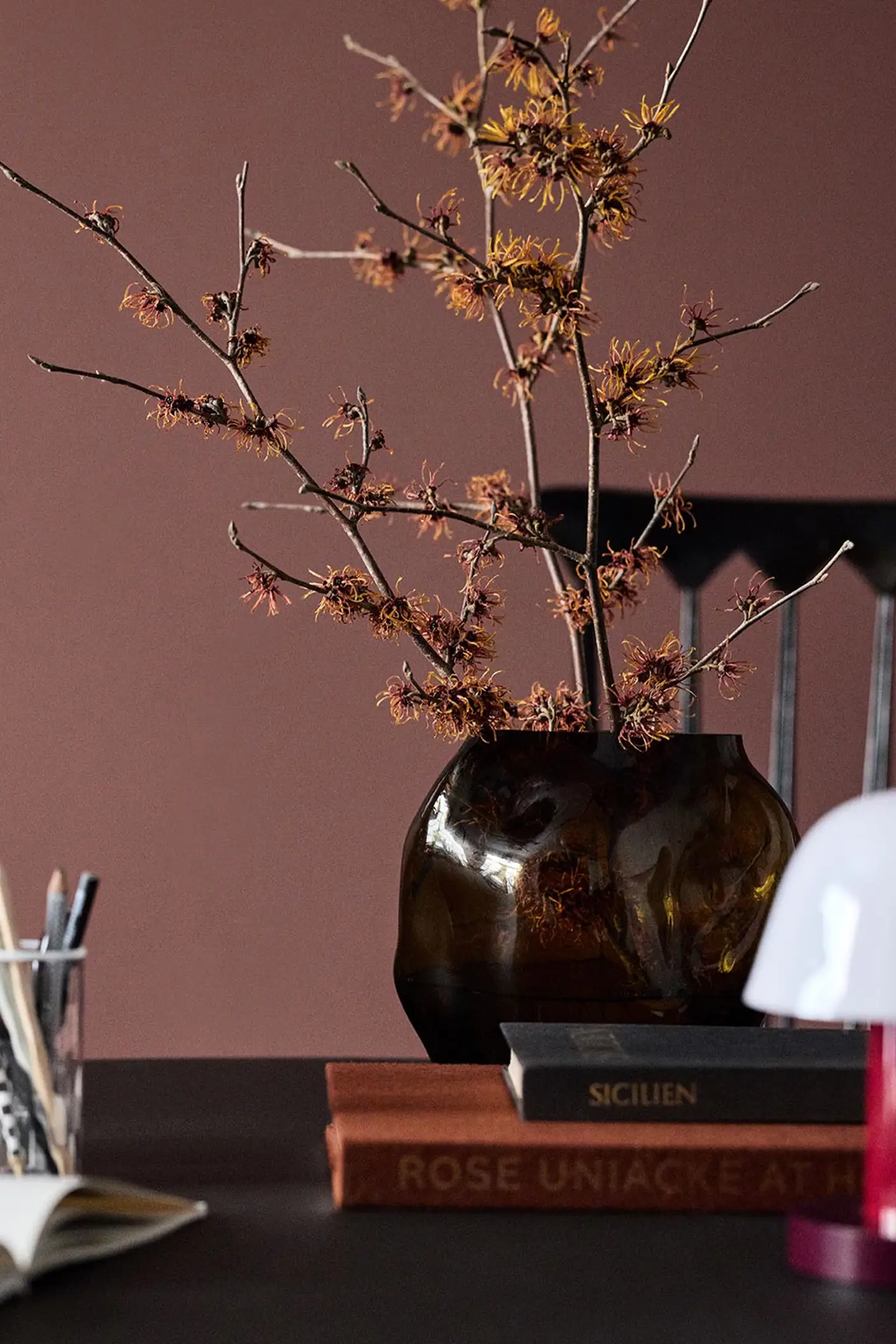 A glass vase on a table set against a deep red wall painted in the colour 2951 Sophisticated Red from Jotun.