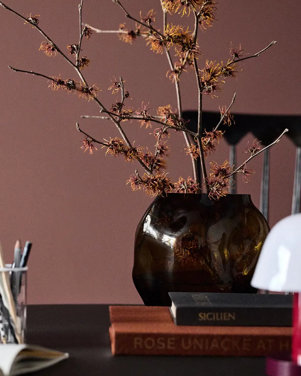 A glass vase on a table set against a deep red wall painted in the colour 2951 Sophisticated Red from Jotun.