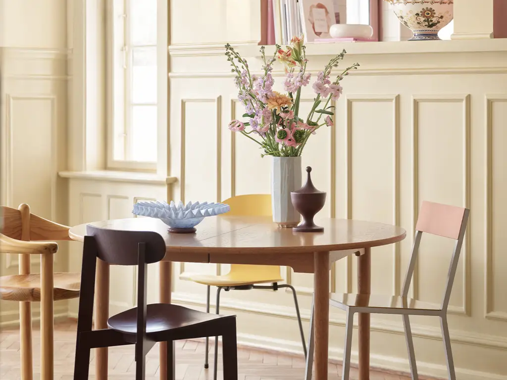 Elegant spiseplass med rundt trebord, ulike designstoler og vase med blomster i lyst, klassisk interiør