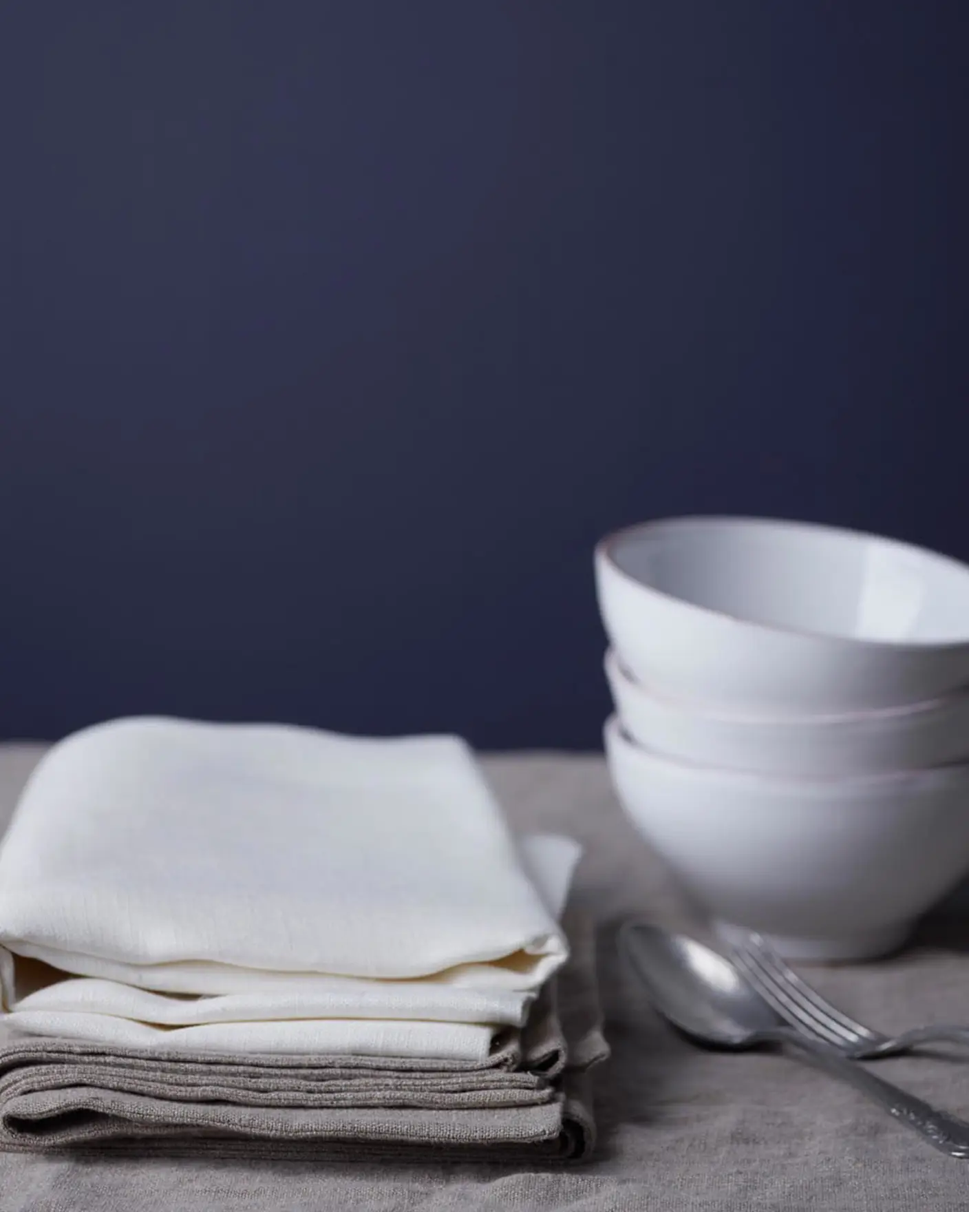 En rödblå vägg, målad med färgen Jotun 4143 Anemon, skapar en lugn bakgrund för en stillsam dukning med vikta linneservetter, staplade vita skålar och enkelt silverbestick.
