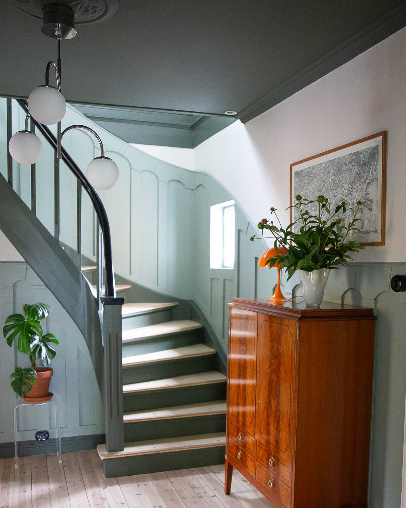 Hall med brystningspanel malt i lys grønn med Jotun LADY Treasure, pussede lyse tregulv, klassisk trapp og tak med kraftig listverk, alt malt i mørkegrønne Jotun Northern Mystic. Vegger mellom tak og brystningspanel malt beige i fargen Jotun Sans.