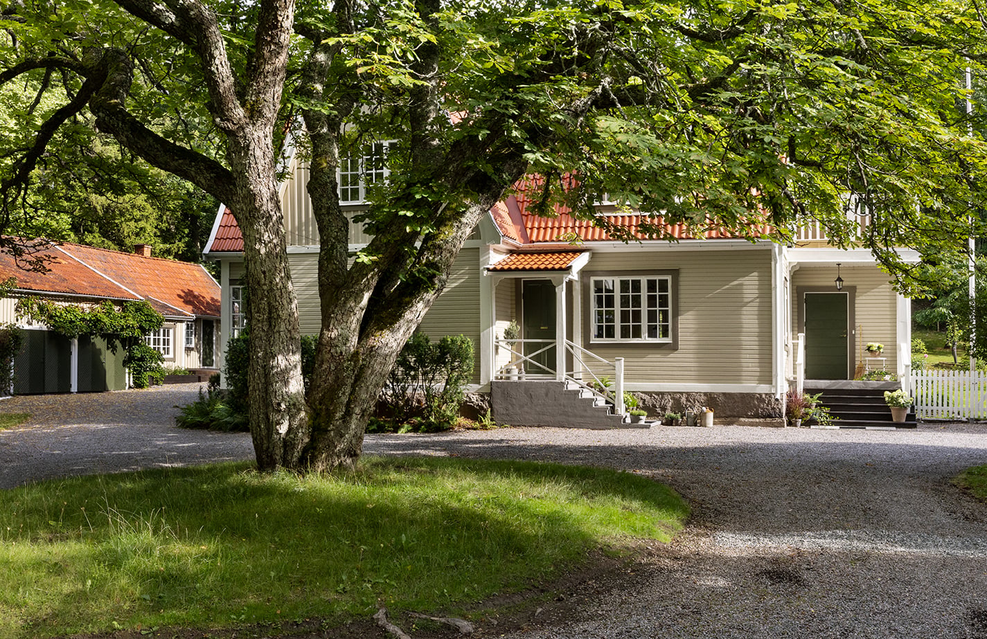 Traditionellt svenskt trähus med rött tak, grusuppfart och stor trädgård omgiven av grönska