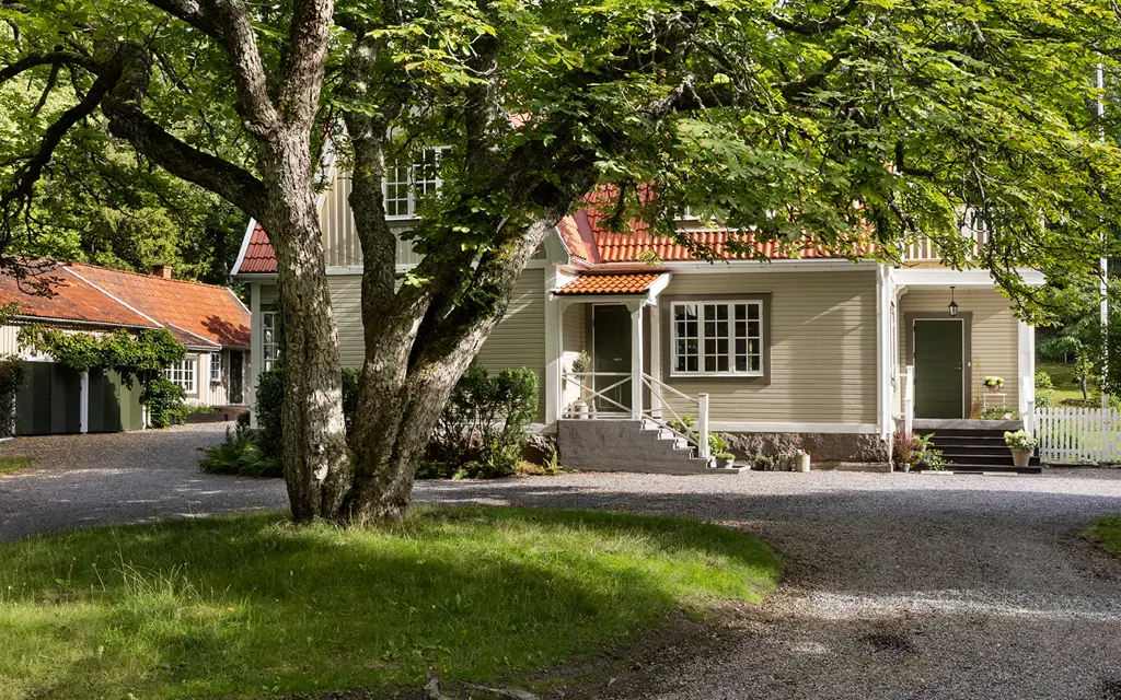 Traditionellt svenskt trähus med rött tak, grusuppfart och stor trädgård omgiven av grönska