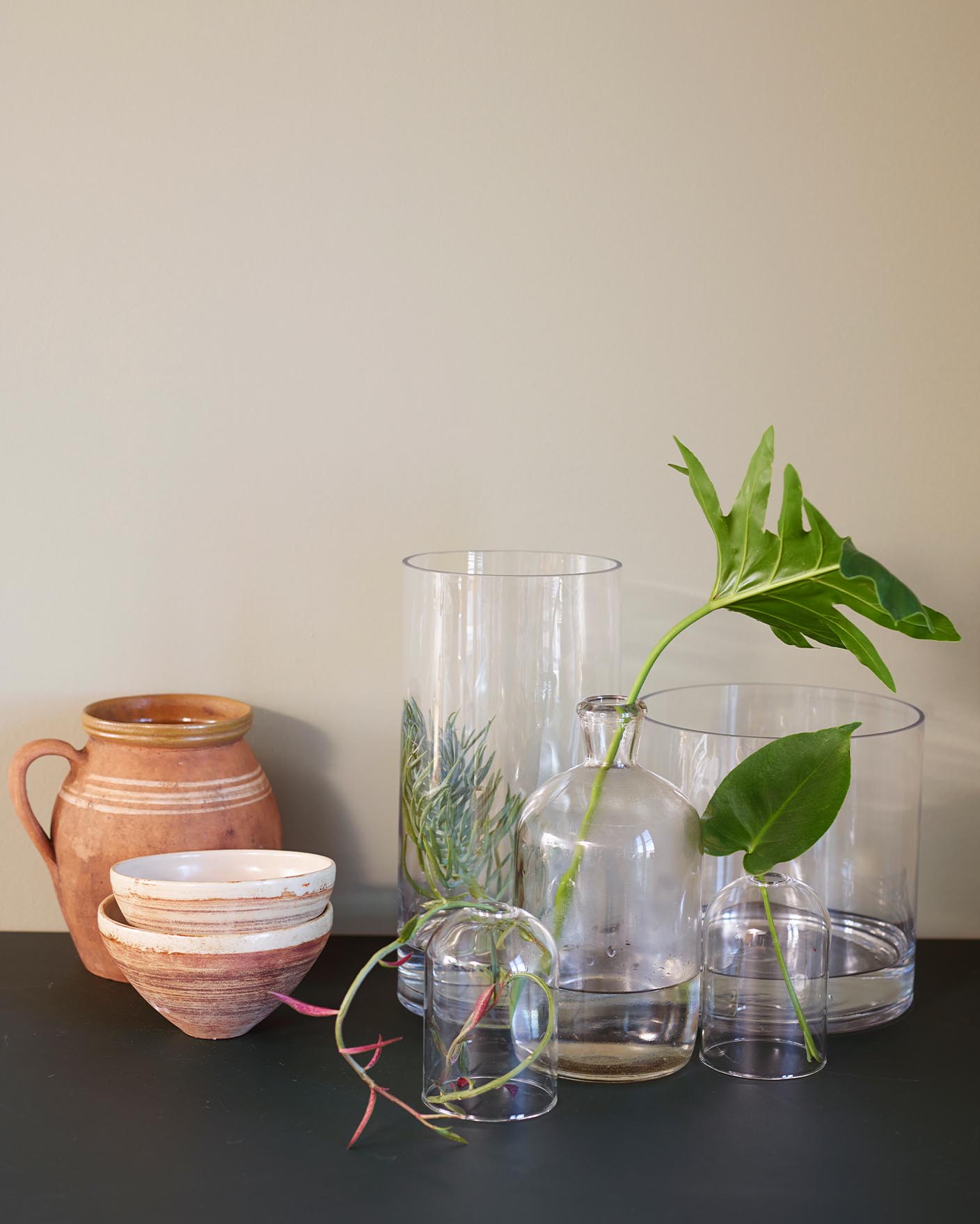 Glass- og keramikkbeholdere på en mørk overflate mot en dempet beige vegg malt med fargen 10679 Washed Linen fra Jotun.