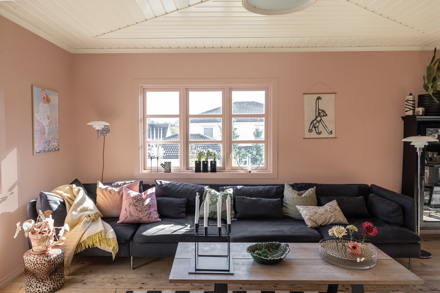 Stue med mørk grå sofa med puter i lyse toner, rosa vegger og vinduskarmer malt i Jotun Pink Ambience, tak i beige Jotun Soft Dunes.