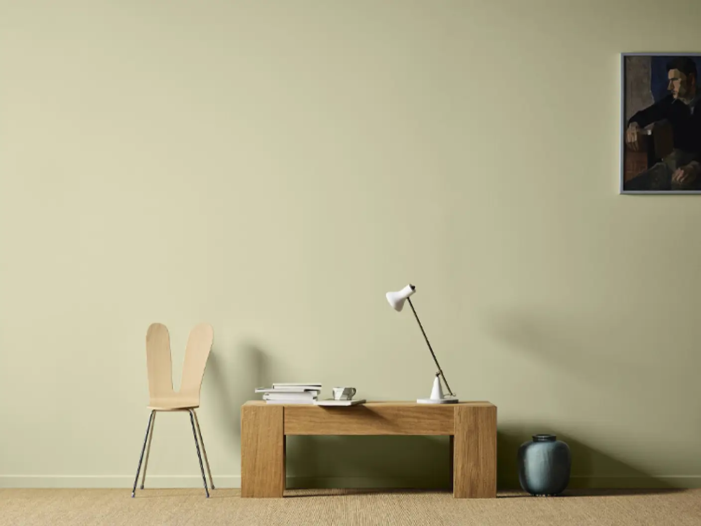 Bord i eik med en hvit lampe og en moderne stol ved siden av, alt mot en lys grønn vegg malt i Jotun Sunny Green