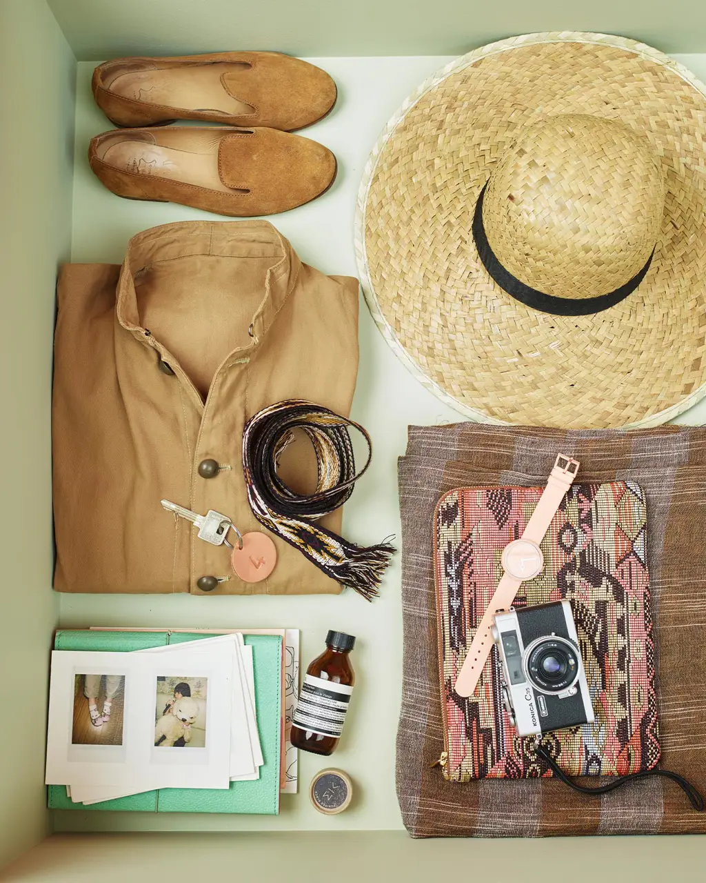 A pair of shoes, straw hat, folded shirt, woven belt, vintage camera and personal accessories, arranged neatly a drawer painted with 8222 Jurrasic Grey, a yellowish green colour from Jotun.
