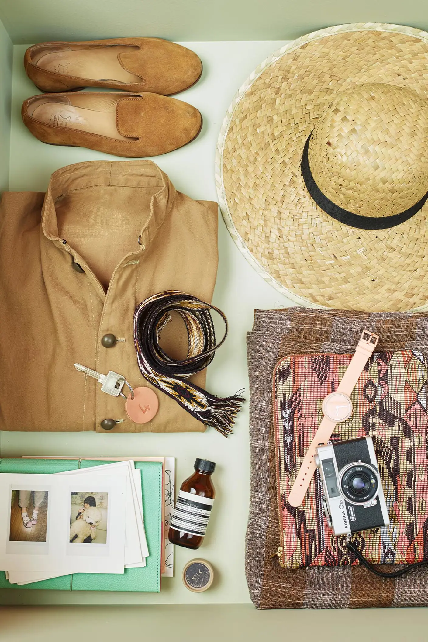 Et par sko, stråhatt, brettet skjorte, vevd belte, vintage kamera og personlige tilbehør, pent ordnet i en skuff malt med 8222 Jurrasic Grey, en gulgrønn farge fra Jotun.