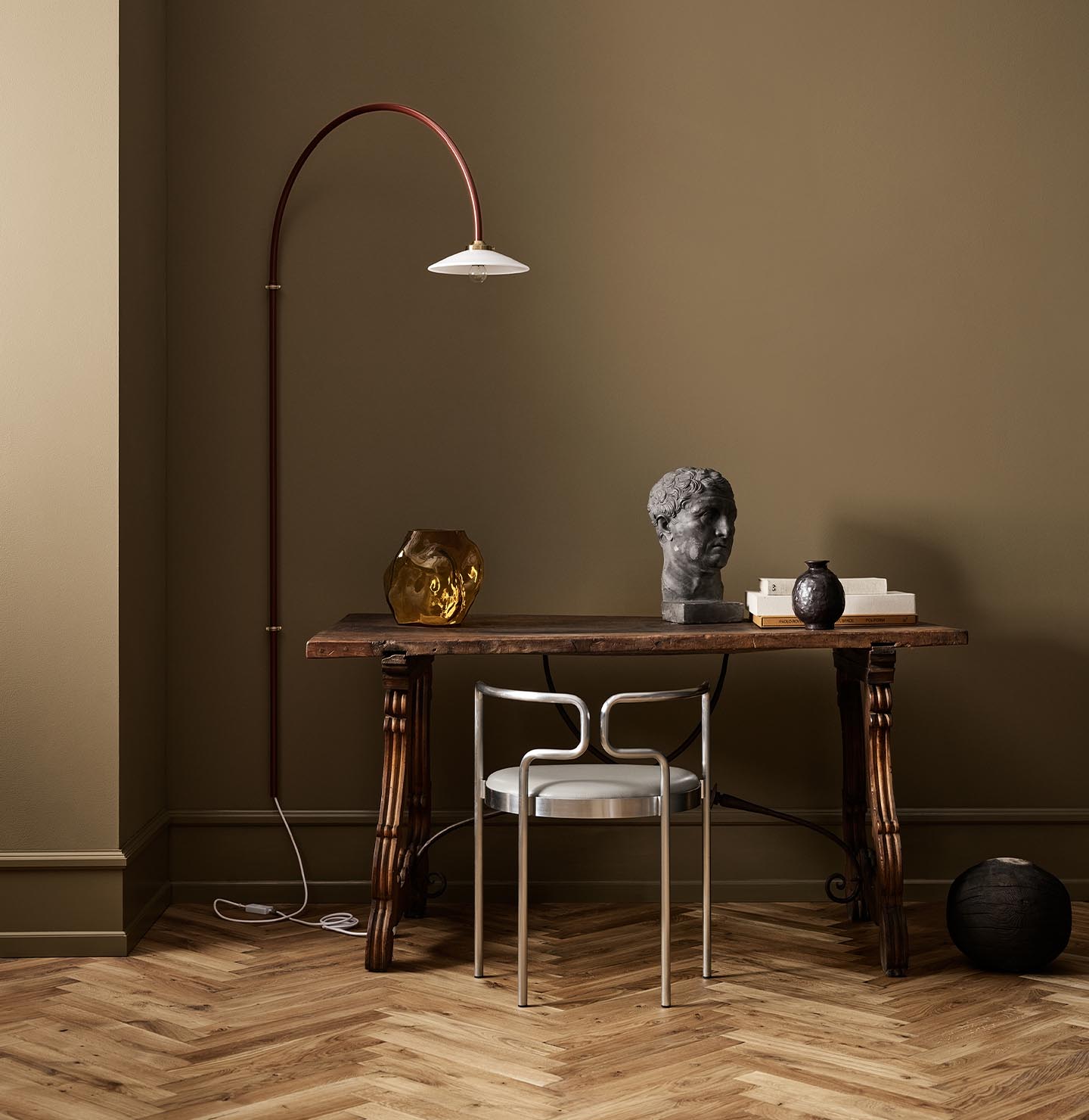 A wooden table, decor, and arched lamp against a golden brown wall in the colour 1974 Golden Walnut from Jotun.