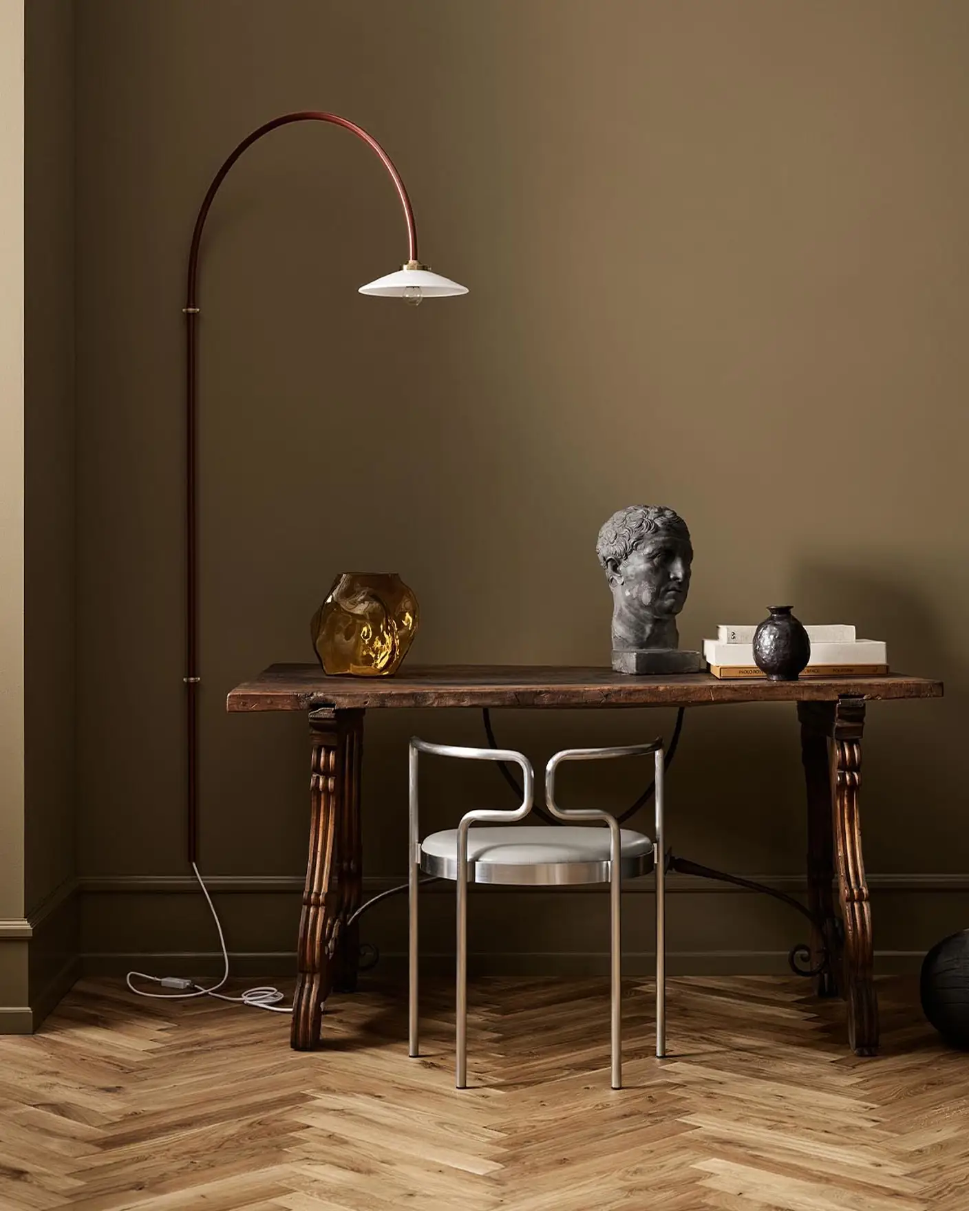 A wooden table, decor, and arched lamp against a golden brown wall in the colour 1974 Golden Walnut from Jotun.