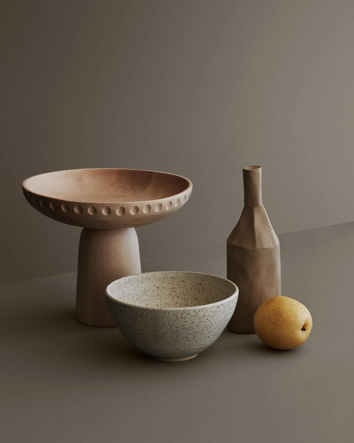 Dämpade gråtoner och jordnära texturer smälter samman i en mjuk, jordnära palett med Jotun 1352 Form som bakgrund. Den matta keramiken och det ljusa träslaget ger en känsla av ro och stilla elegans.