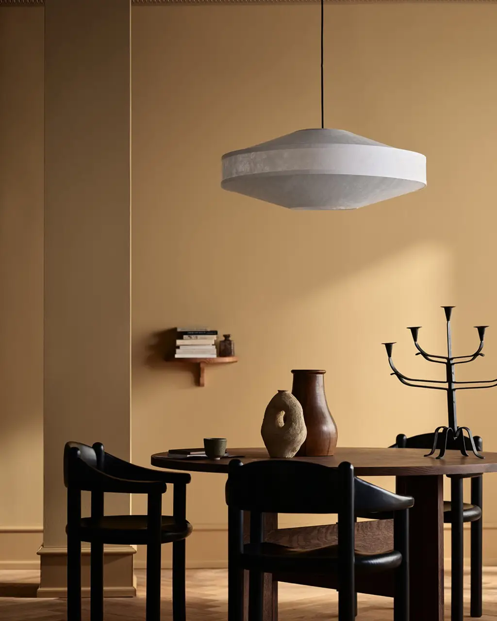 Modern matsal med runt träbord, svarta stolar, designlampa och dekorativa vaser i varm beige inredning. Väggar målade i Jotun 1909 Kalkockra och lister i Jotun 1799 Spice Brown.