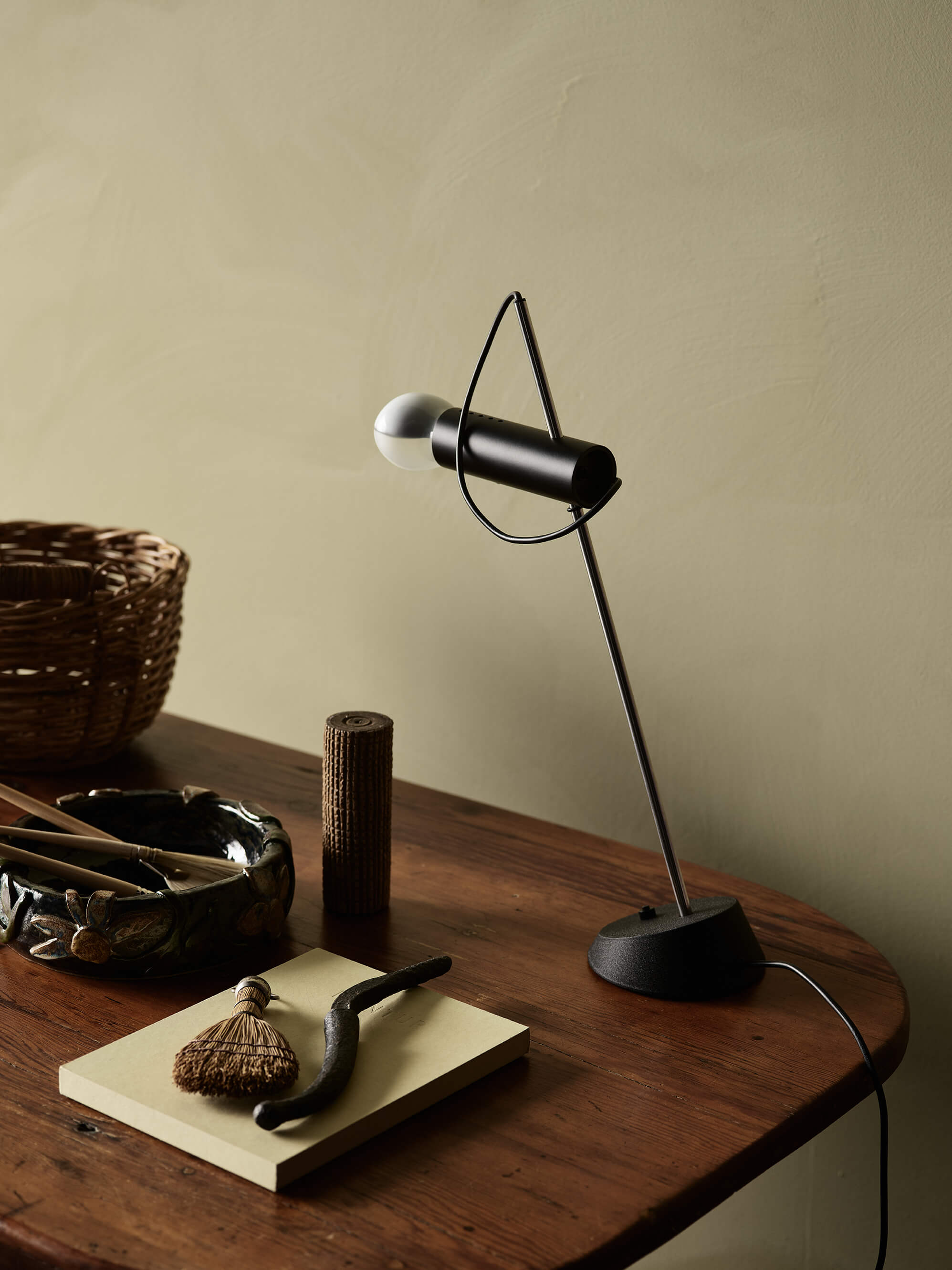 Et hjemmekontor med kalkmalede olivengrønne vægge i Jotun 0290 Biri fra LADY Minerals, et skrivebord i træ med en sort bordlampe samt rustikke genstande, der tilfører rummet varme og karakter.
