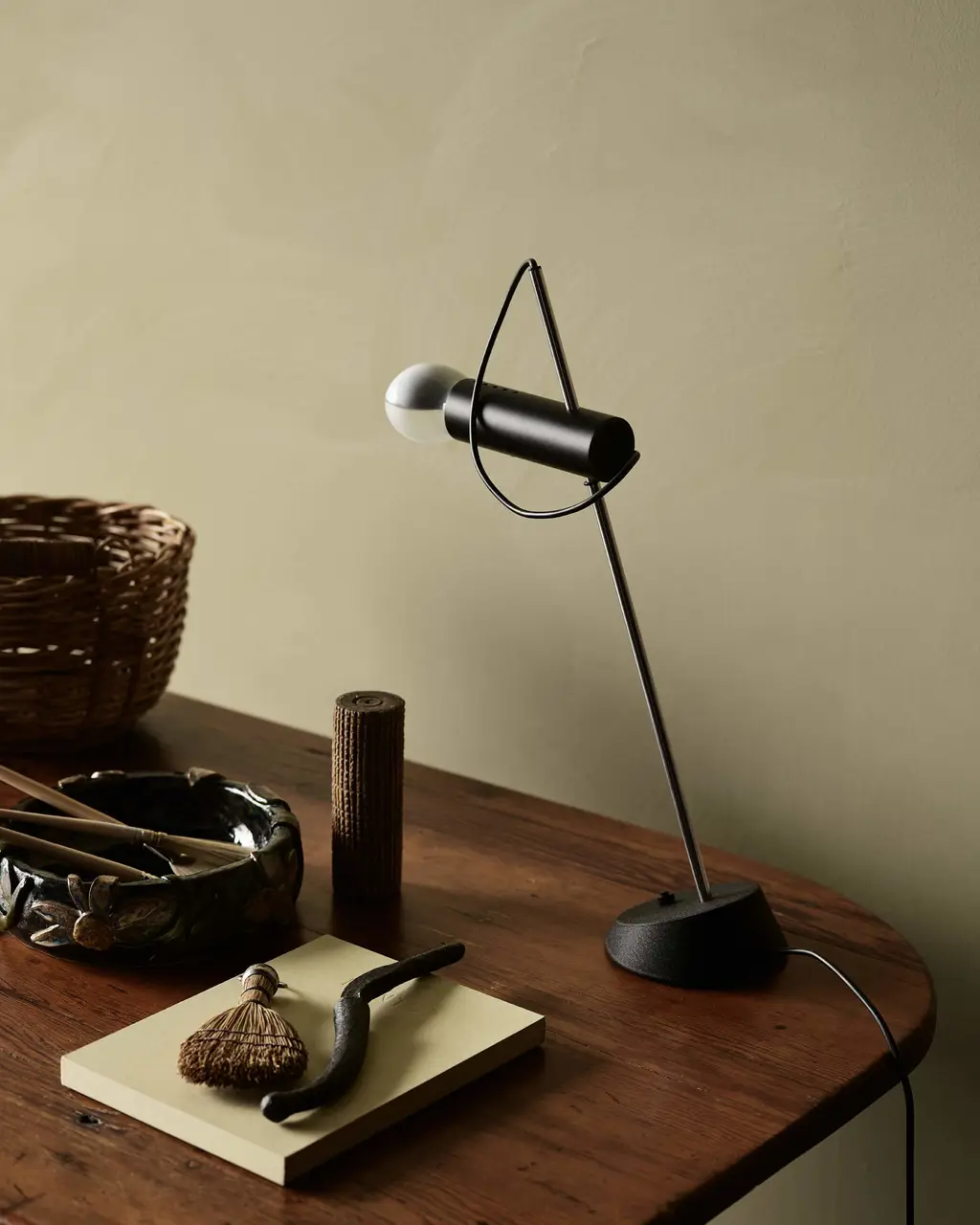 Et hjemmekontor med kalkmalede olivengrønne vægge i Jotun 0290 Biri fra LADY Minerals, et skrivebord i træ med en sort bordlampe samt rustikke genstande, der tilfører rummet varme og karakter.