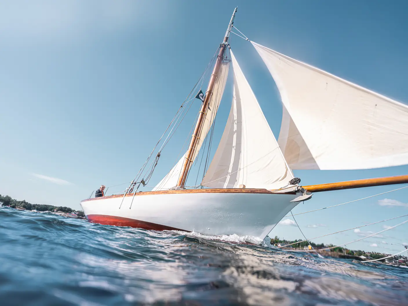 Seilbåt med hvite seil på stille sjø med blå himmel bak